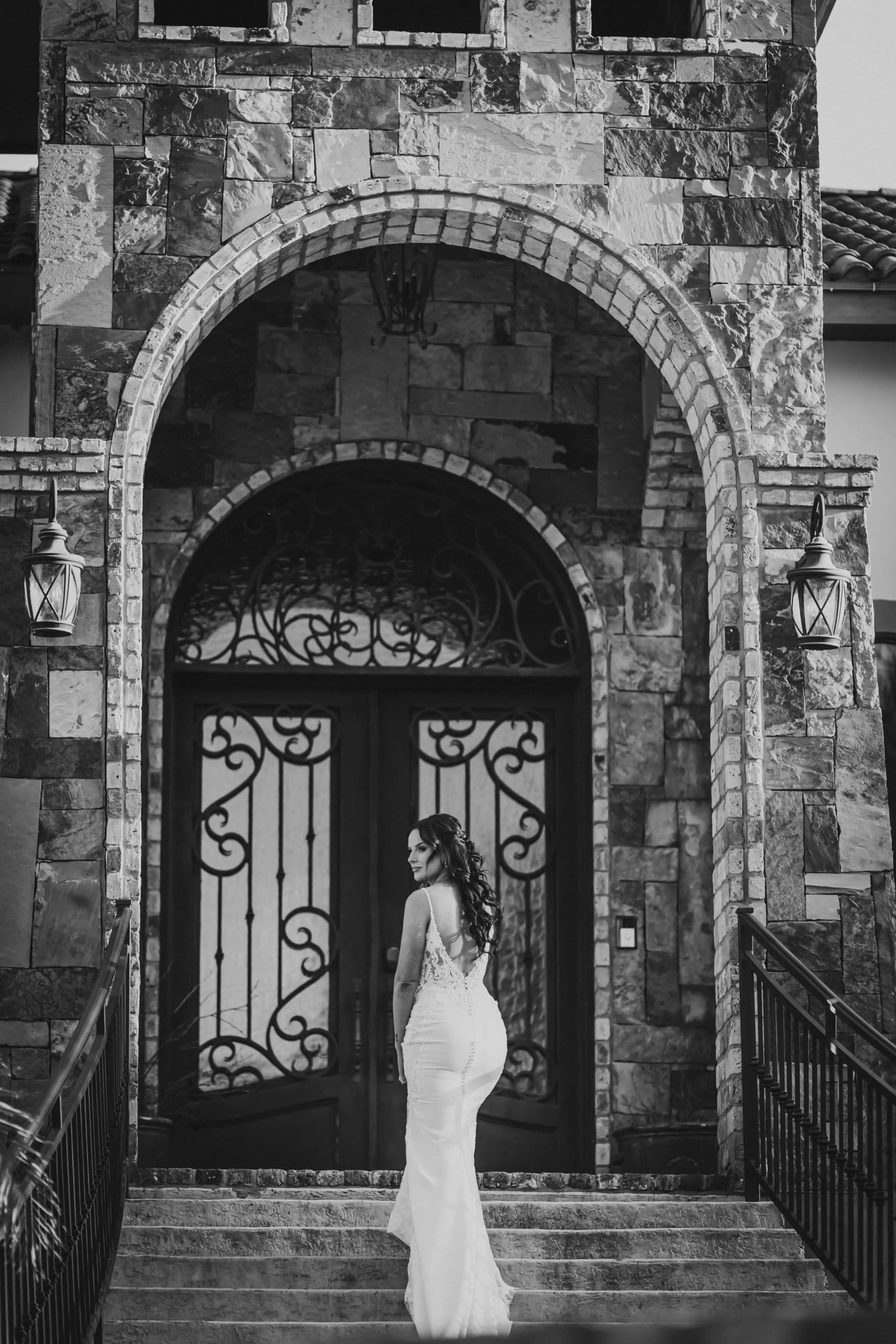 A woman in a white dress stands on steps leading to a grand stone entrance with intricate doors.