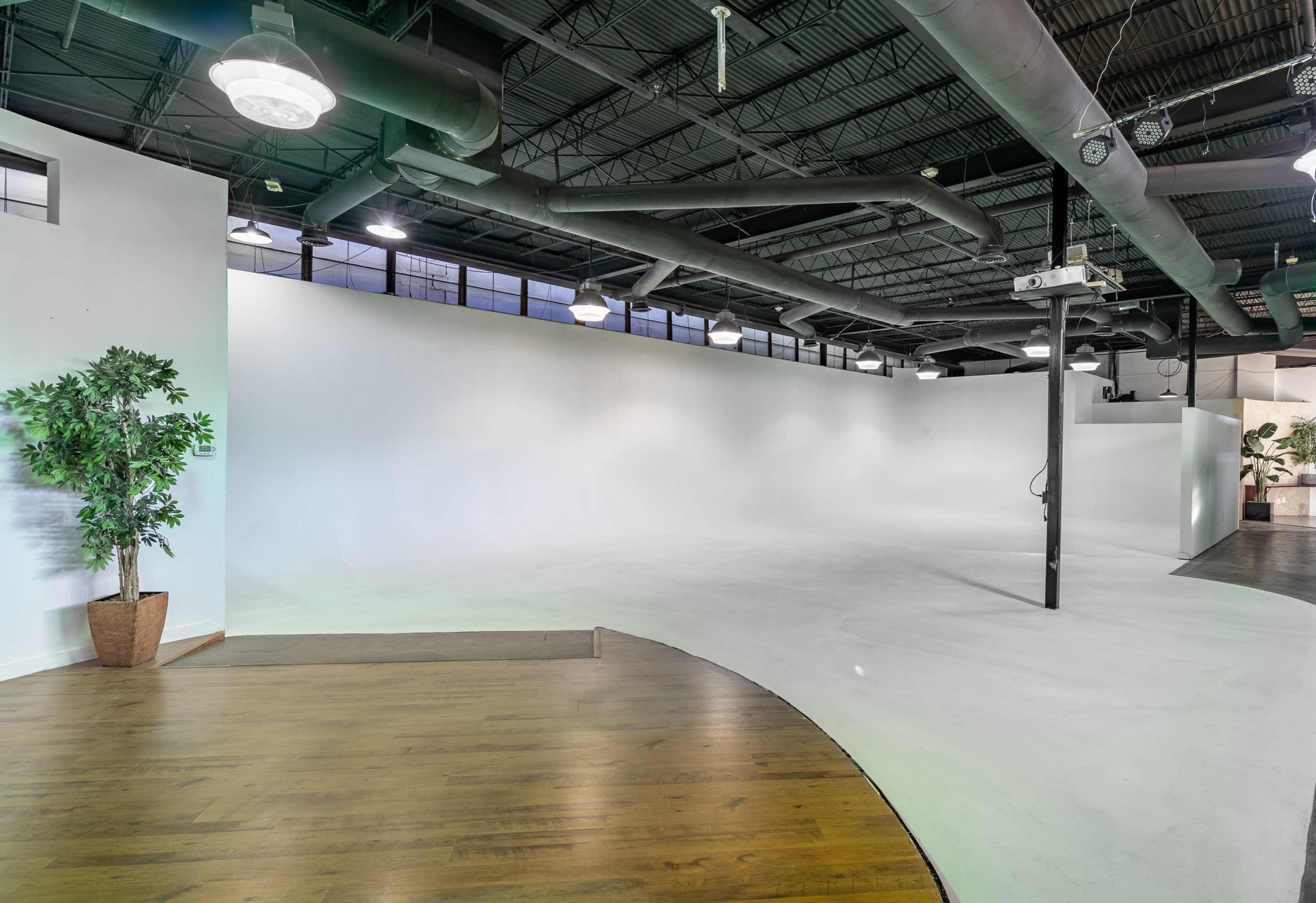 A spacious interior with a curved wooden floor, a large white wall, and industrial-style ceiling features.