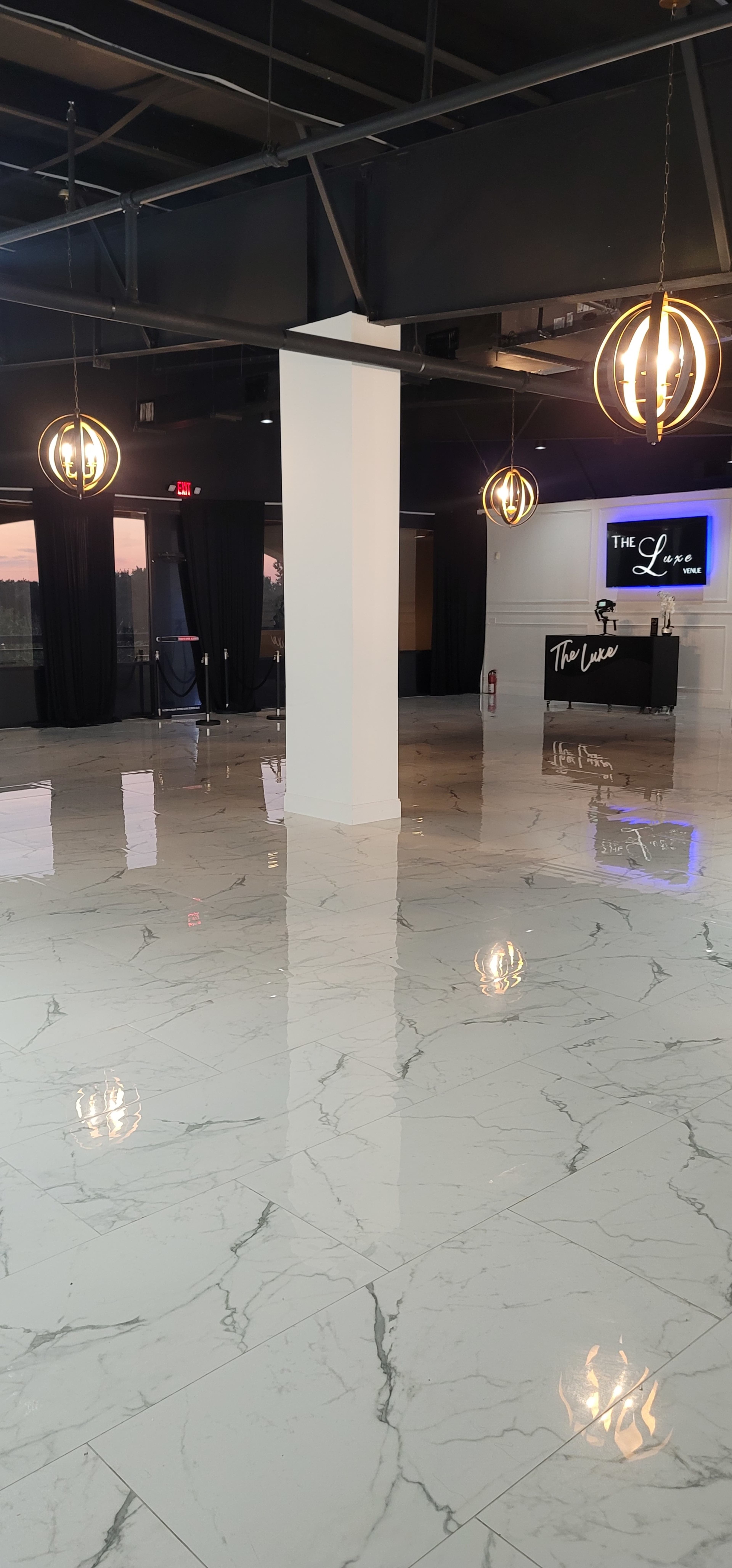 An empty venue with marble flooring, elegant lighting fixtures, and a reception area at the back.