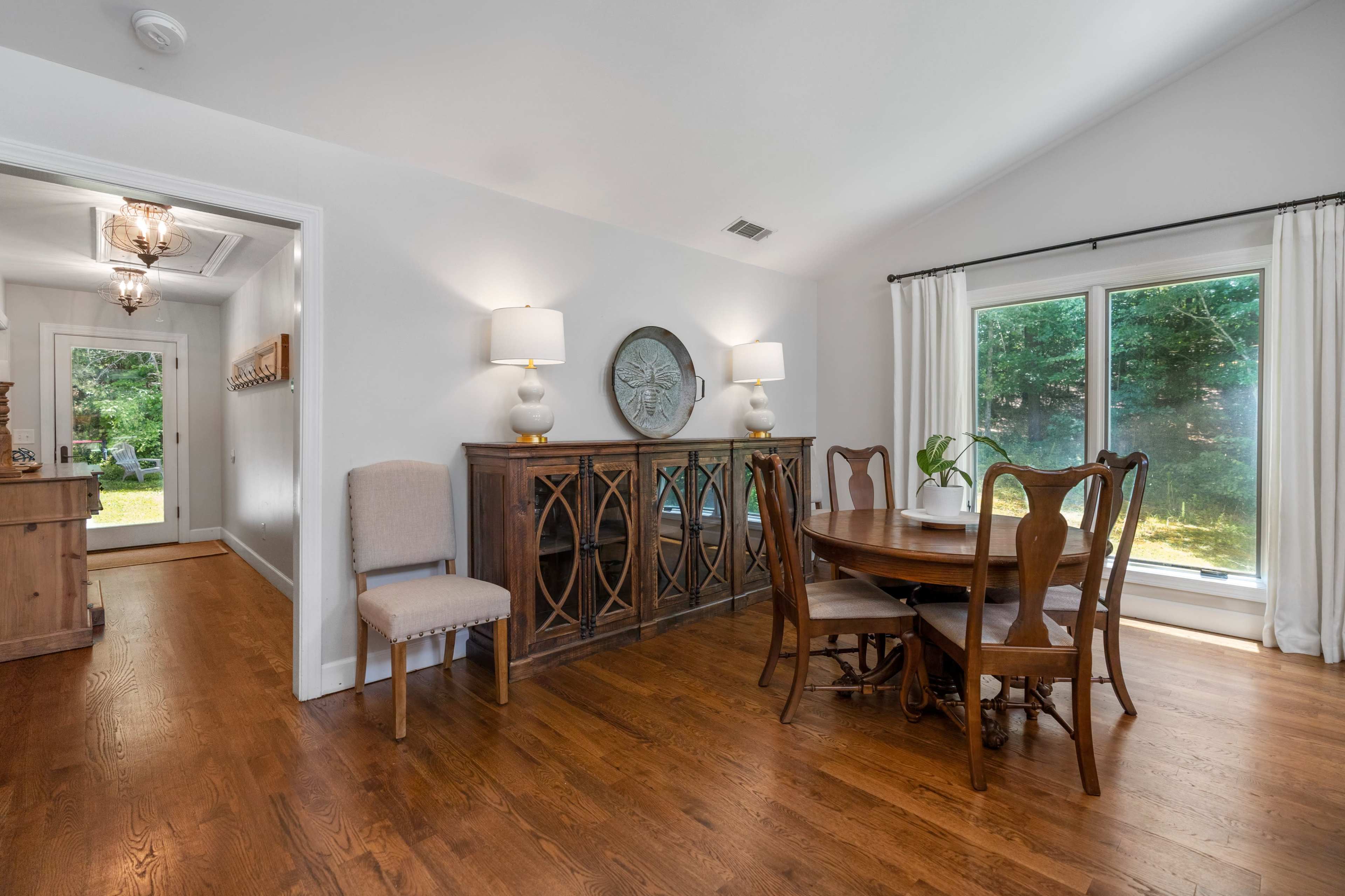 A dining area featuring a wooden table and chairs, a sideboard, and large windows letting in natural light.