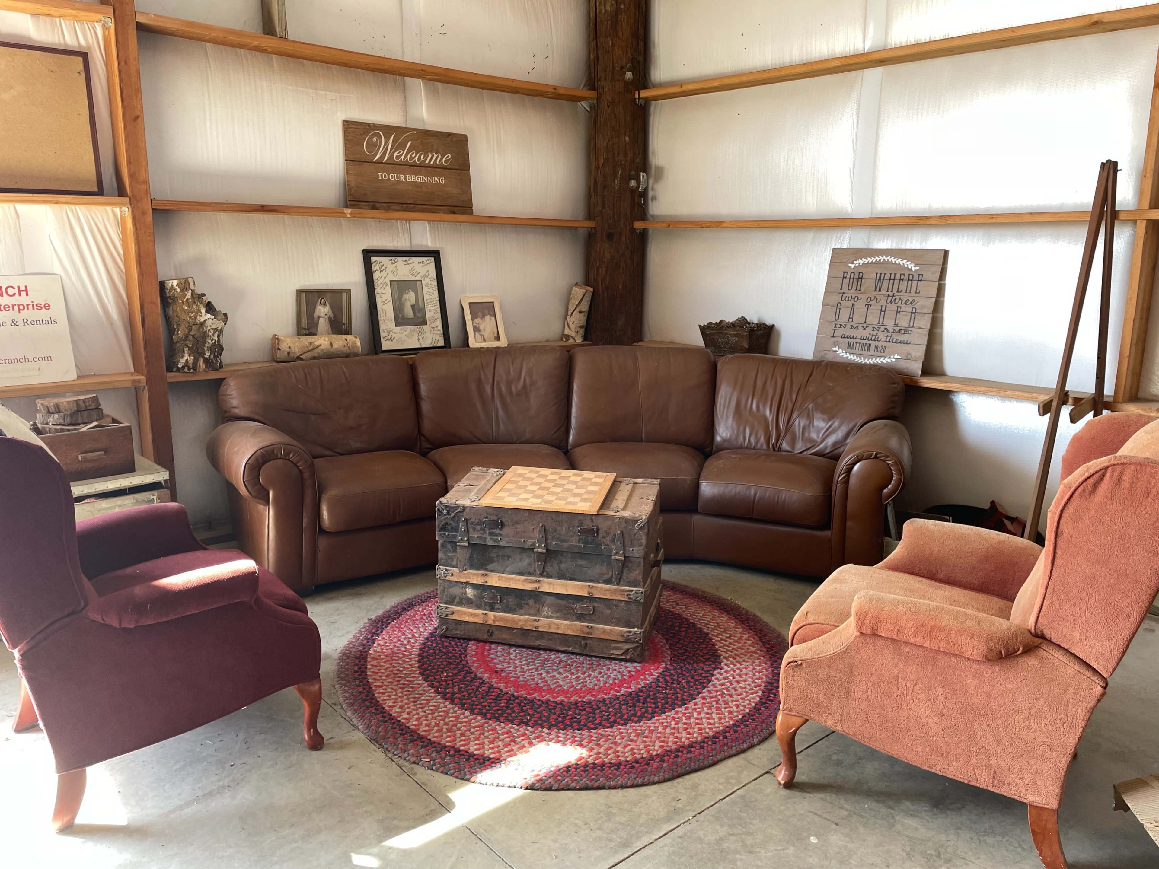 A cozy seating area with a brown leather couch, two armchairs, and a wooden coffee table on a circular rug in a barn-like setting.