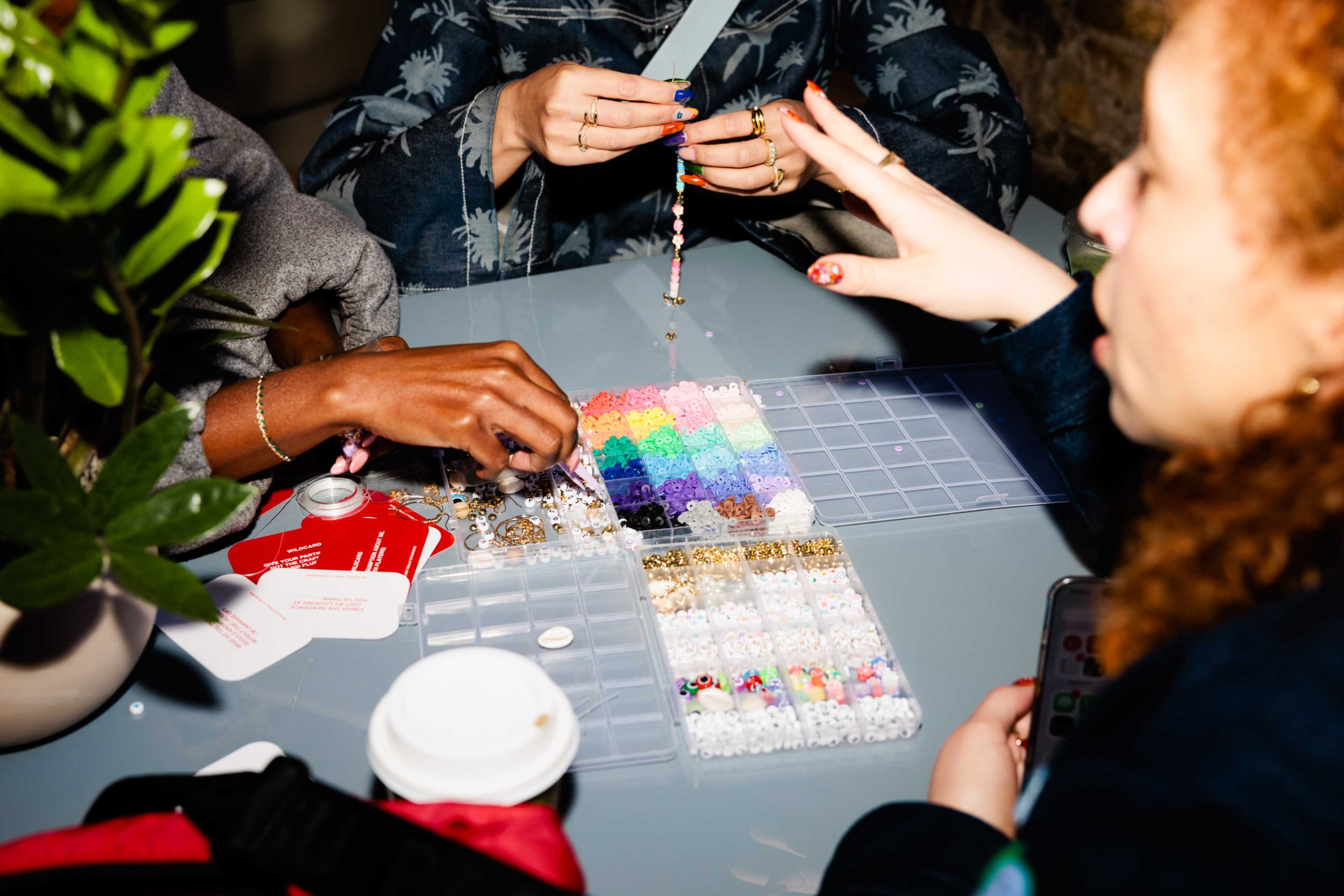 A group of people is crafting jewelry at a table covered with various beads and materials.