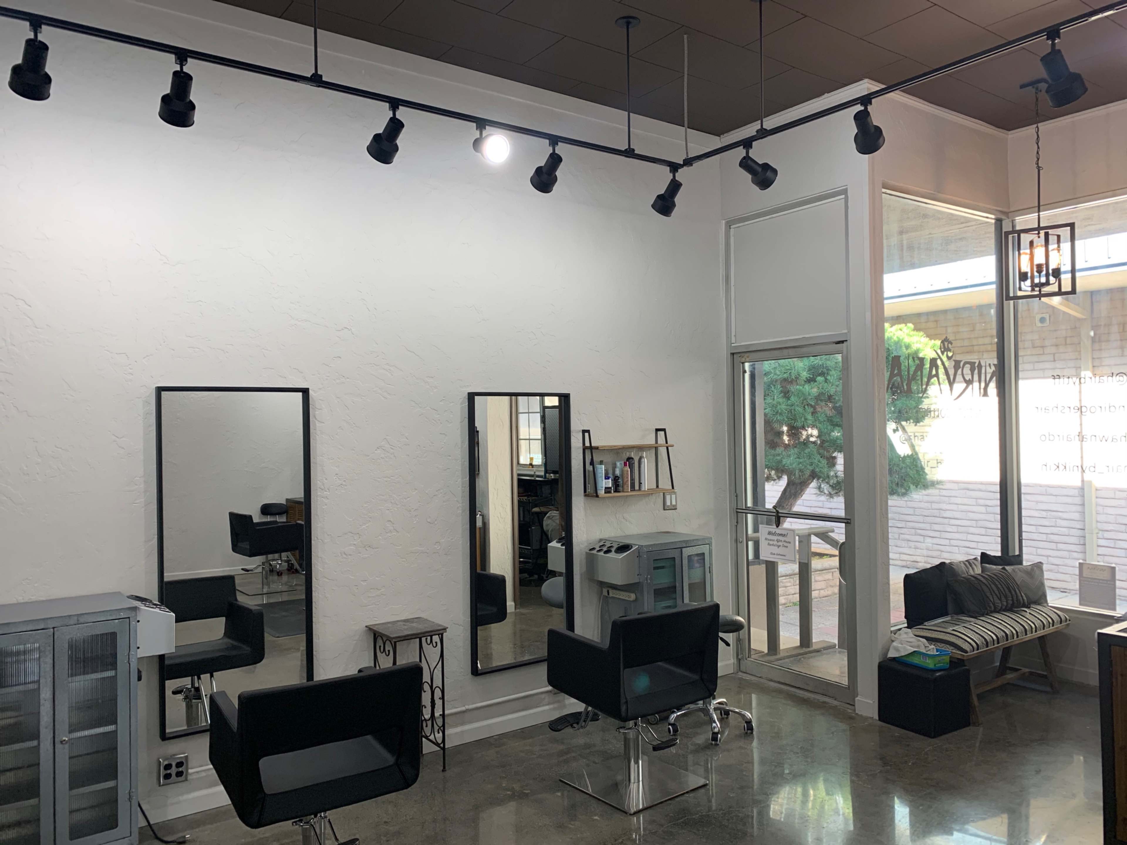 An interior view of a hair salon featuring two large mirrors, black styling chairs, and large windows allowing natural light.