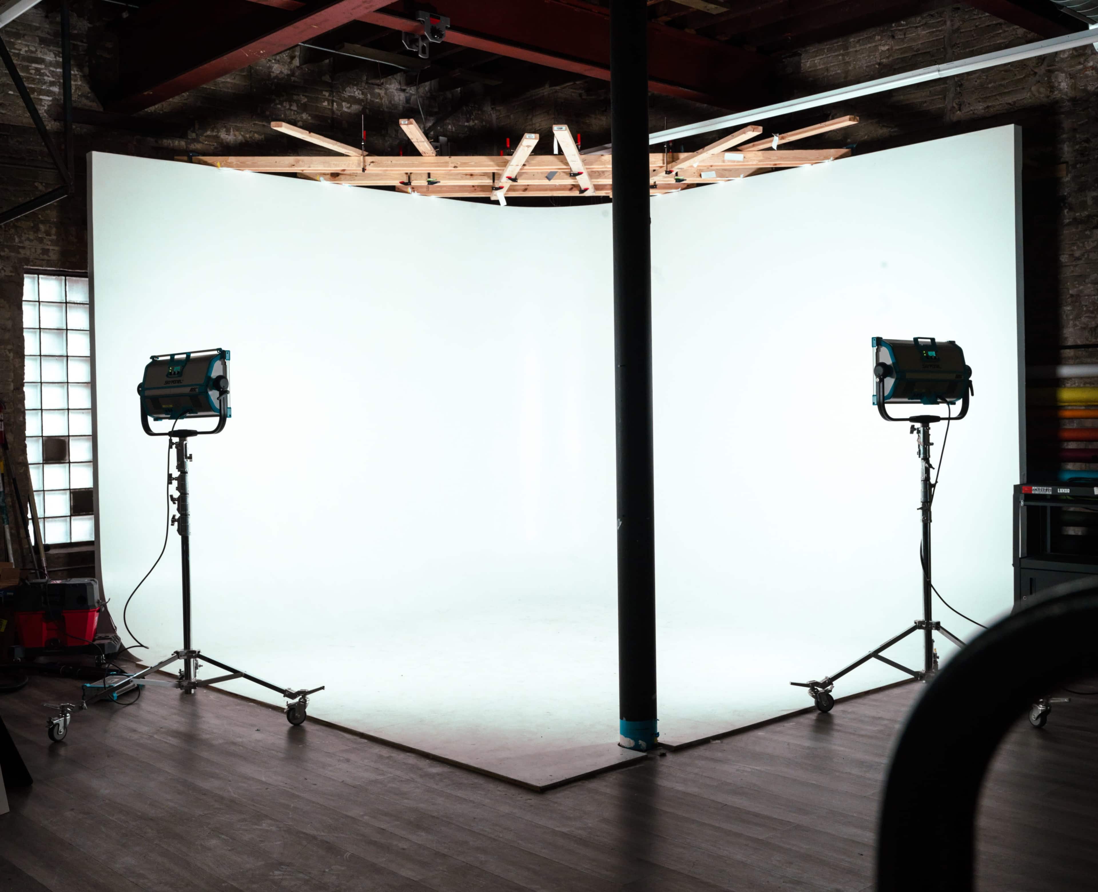 The image shows a photography studio with a blank curved backdrop and two lighting stands positioned on either side.