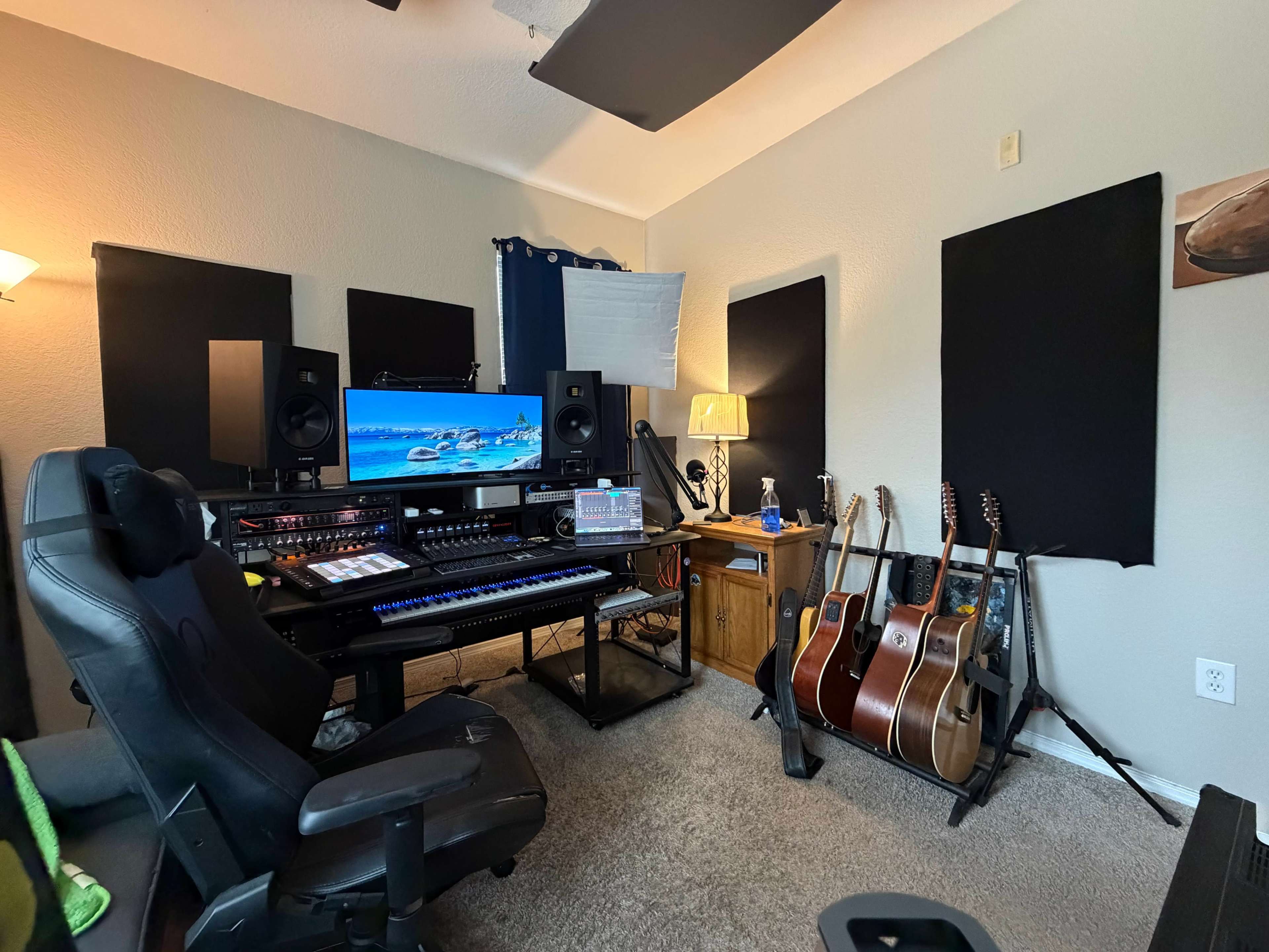 The image depicts a music studio setup with a keyboard, audio equipment, and multiple guitars arranged in a comfortable workspace.