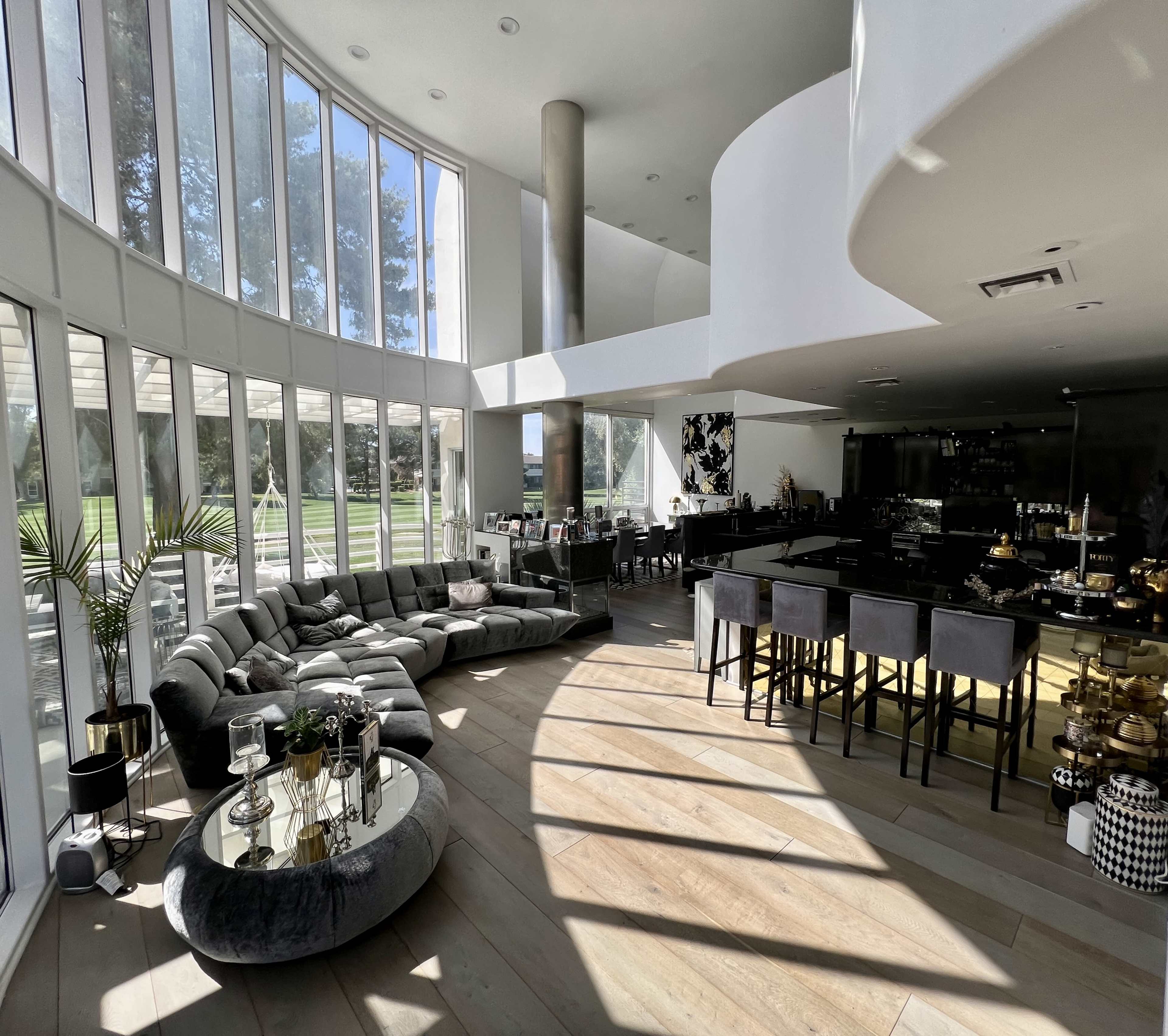 The spacious interior features a sectional sofa and a modern kitchen, illuminated by large windows that overlook a green landscape.