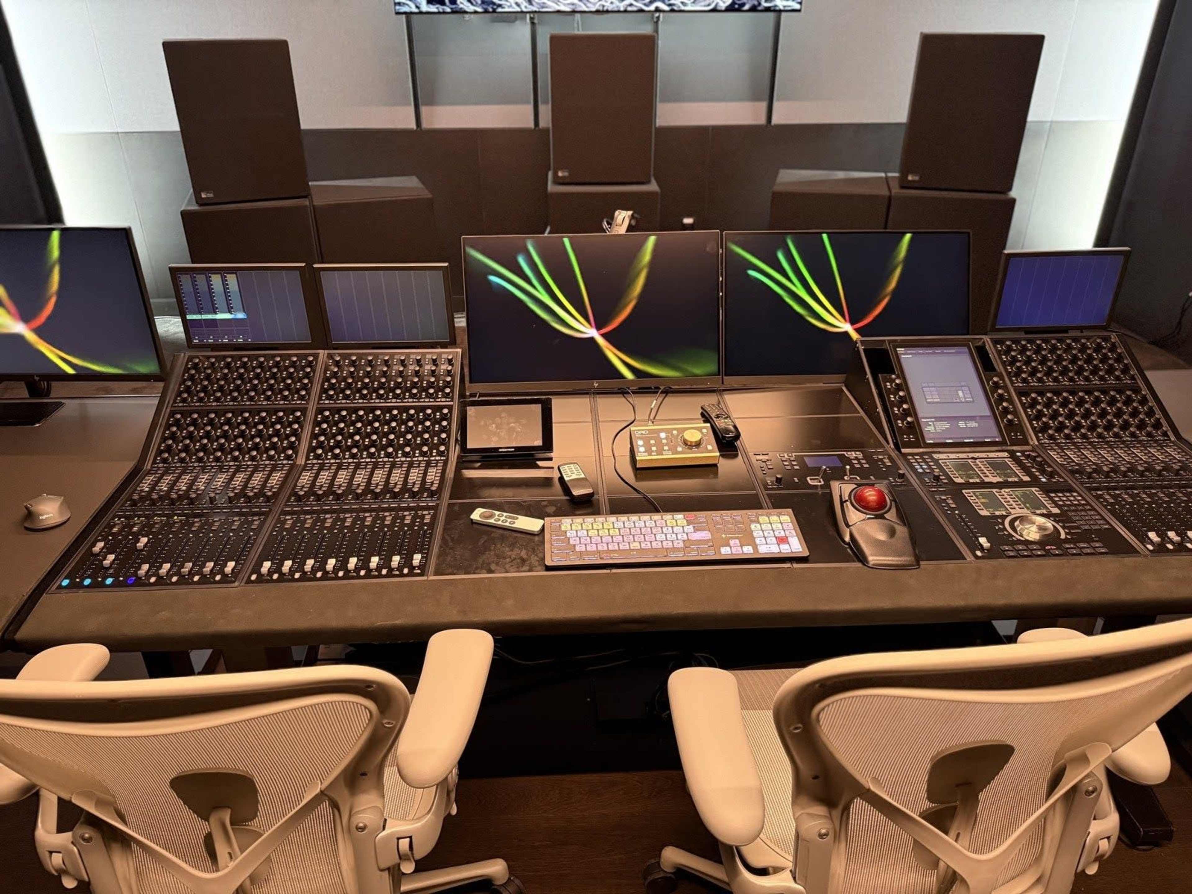 The image shows a modern audio mixing console with multiple monitors and sound equipment in a sleek studio environment.