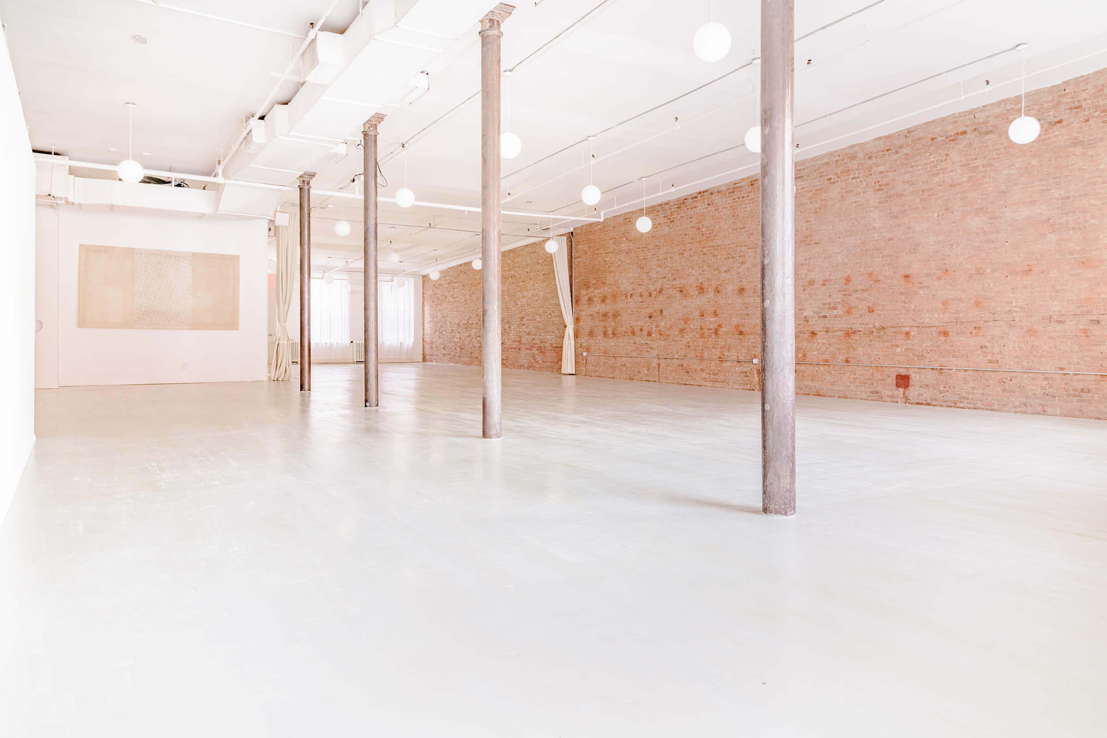 A spacious, empty room with wooden pillars, a light-colored floor, and exposed brick walls.