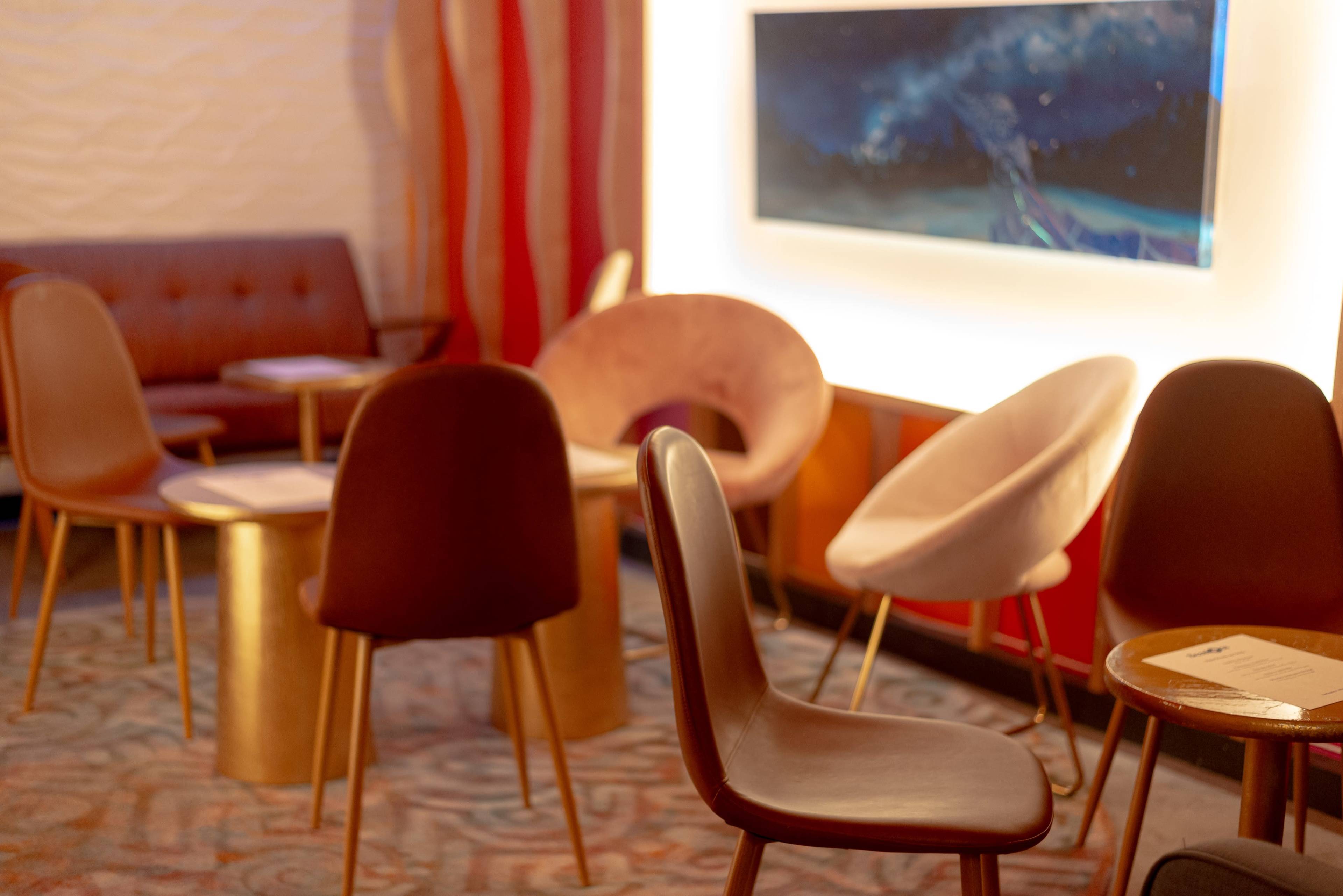 A cozy lounge area features several modern chairs and tables, with a wall-mounted artwork in the background.