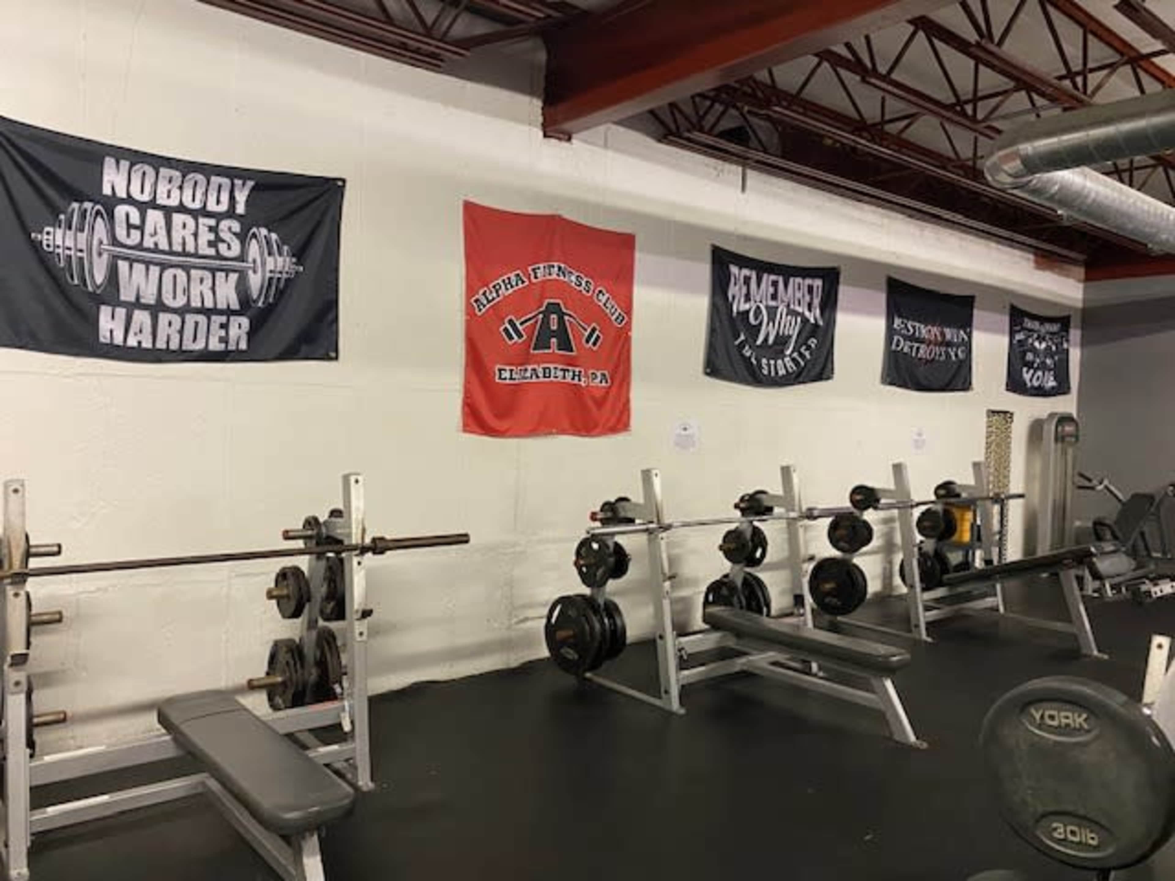A gym interior with weightlifting benches, free weights, and several motivational banners hanging on the wall.