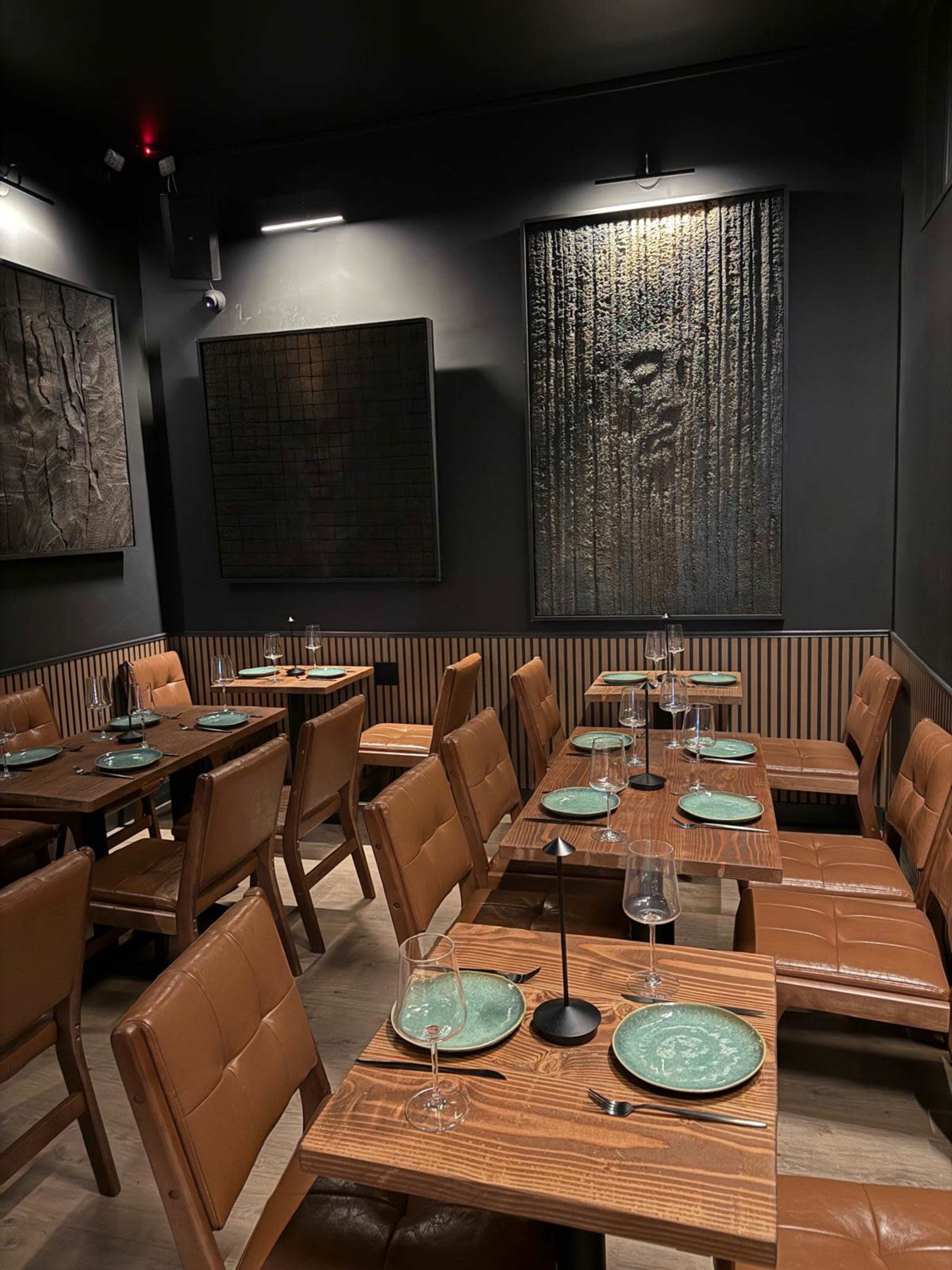 The image shows a dining area with wooden tables and brown leather chairs, featuring green plates and abstract wall art.