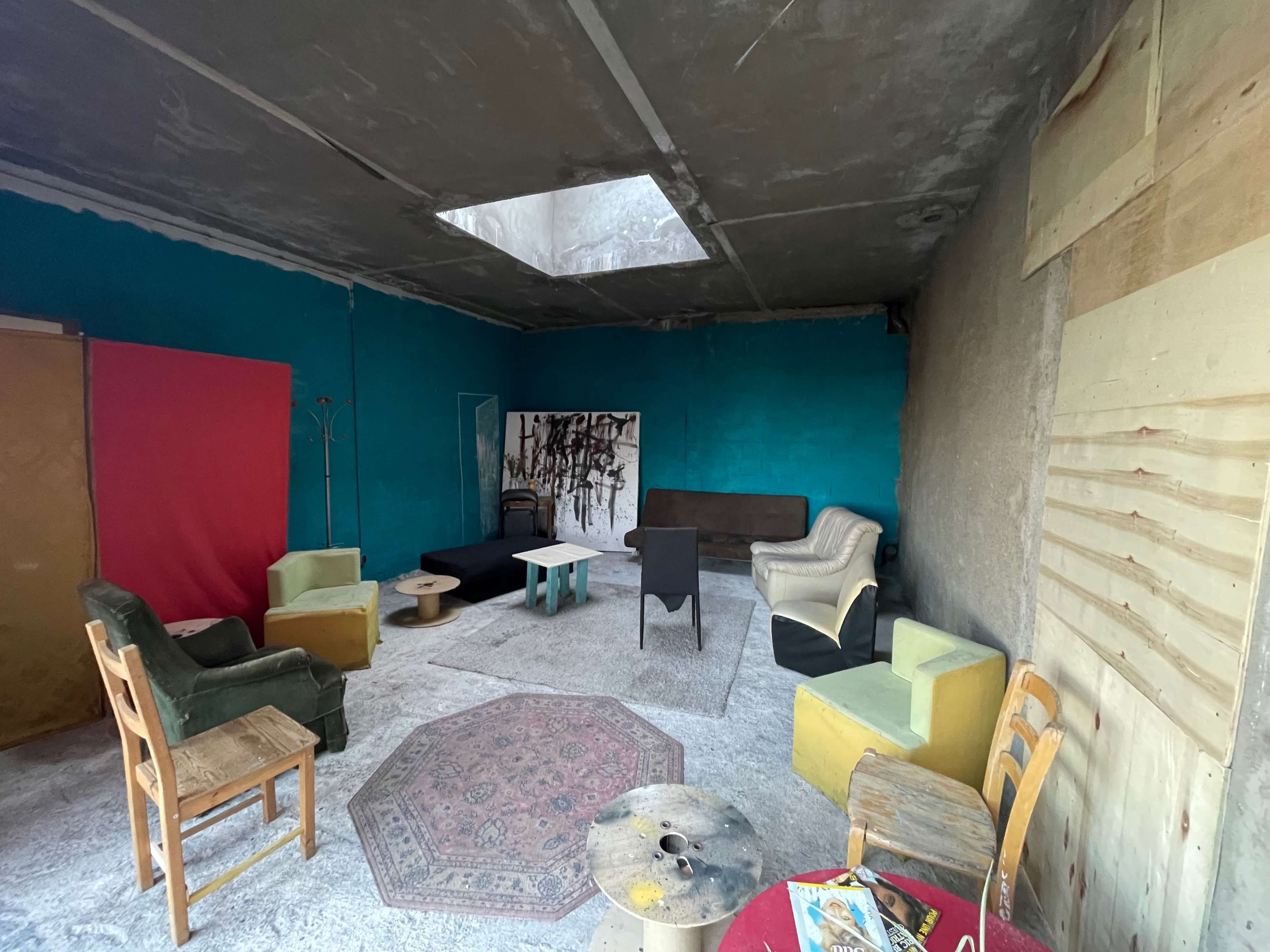 An unfinished room with a bright blue wall, various chairs, a table, and a skylight overhead.