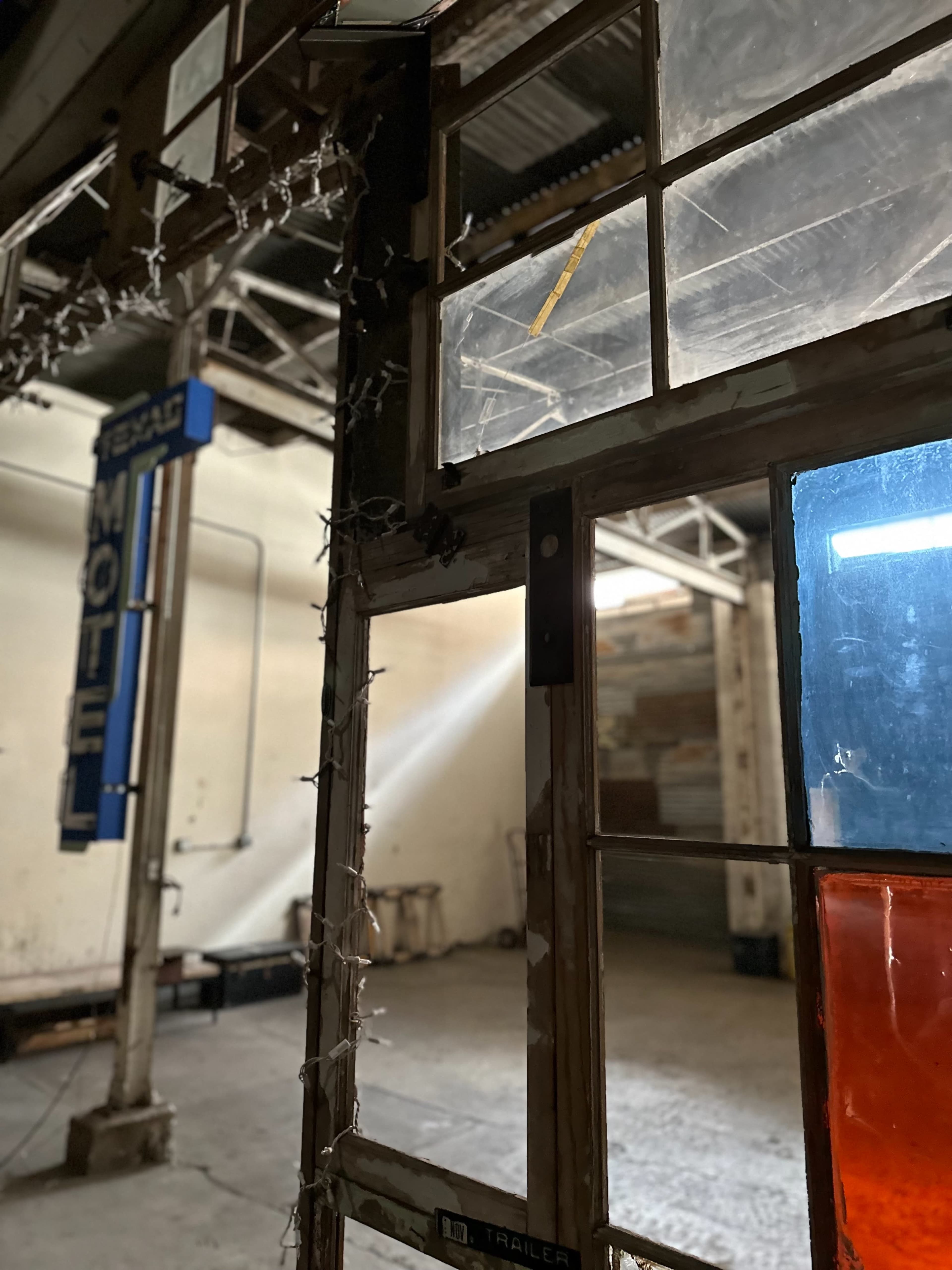 The image shows a partially open door leading into a dimly lit space with a vintage motel sign visible outside.