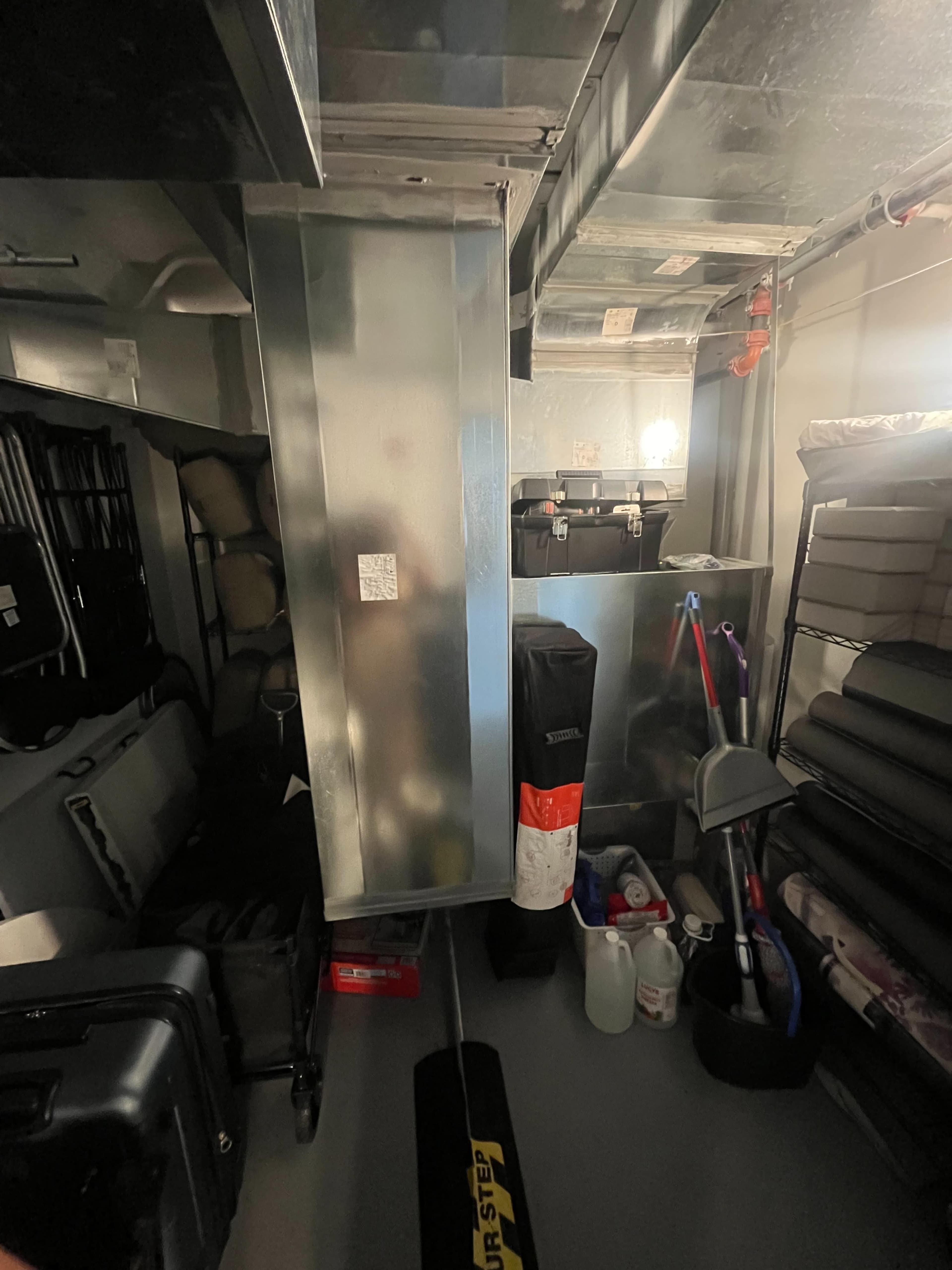 A cluttered garage space with various storage containers, tools, and equipment organized along the walls and a central column.