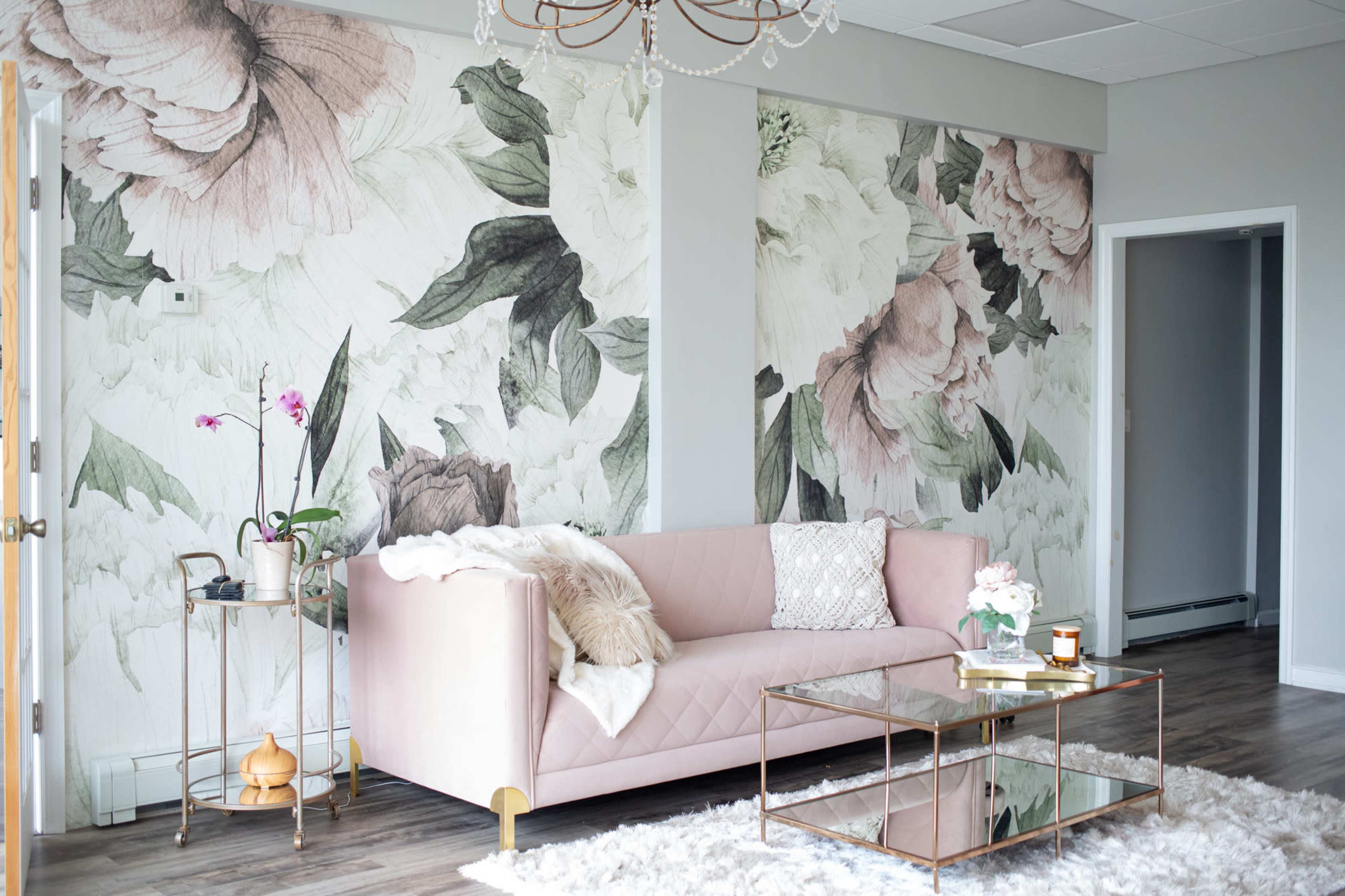 A living room with floral wallpaper, a pink sofa, a glass coffee table, and a decorative plant.