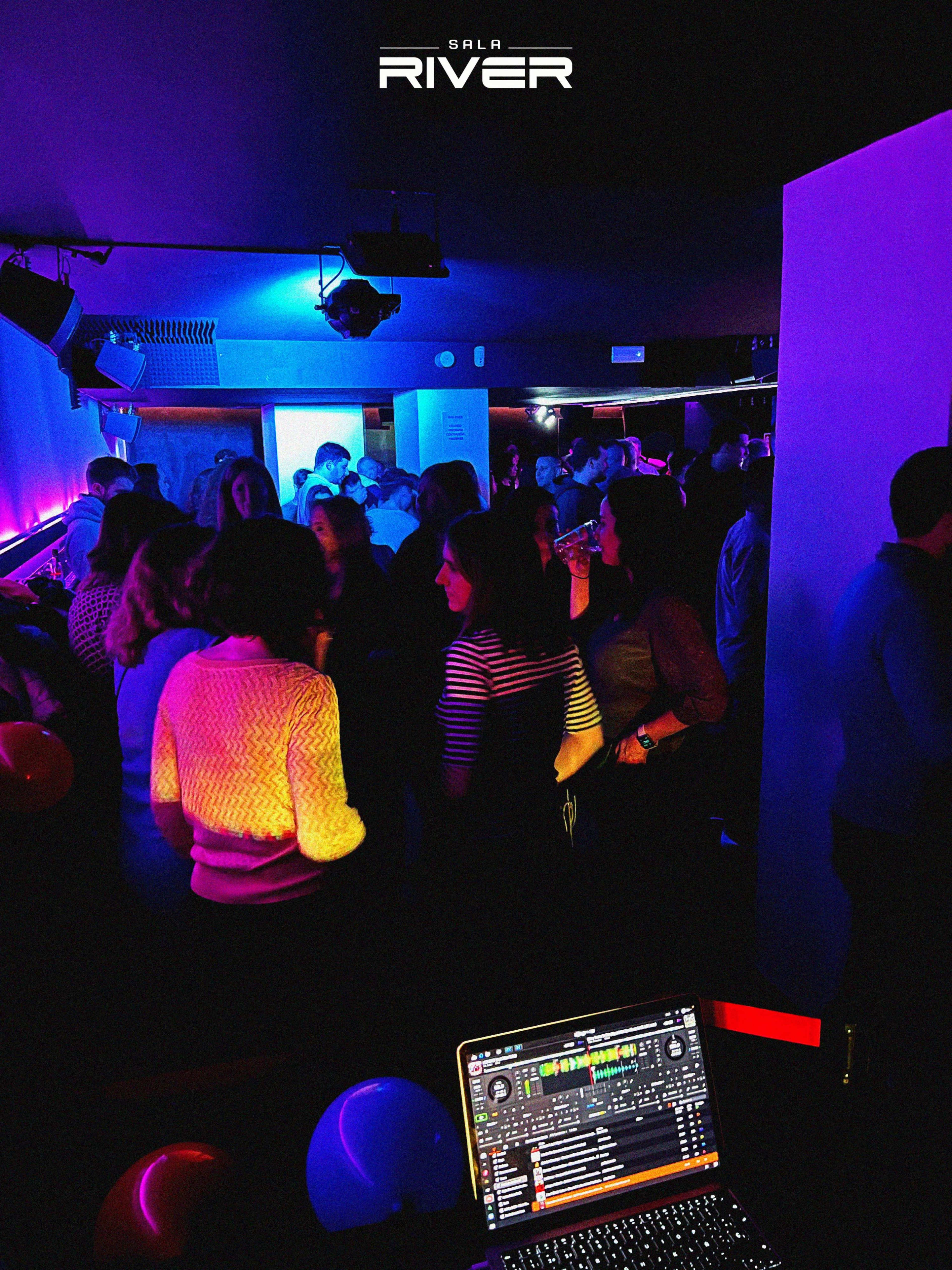 A crowded nightclub scene features partygoers mingling under colorful lighting, with a DJ setup visible in the foreground.