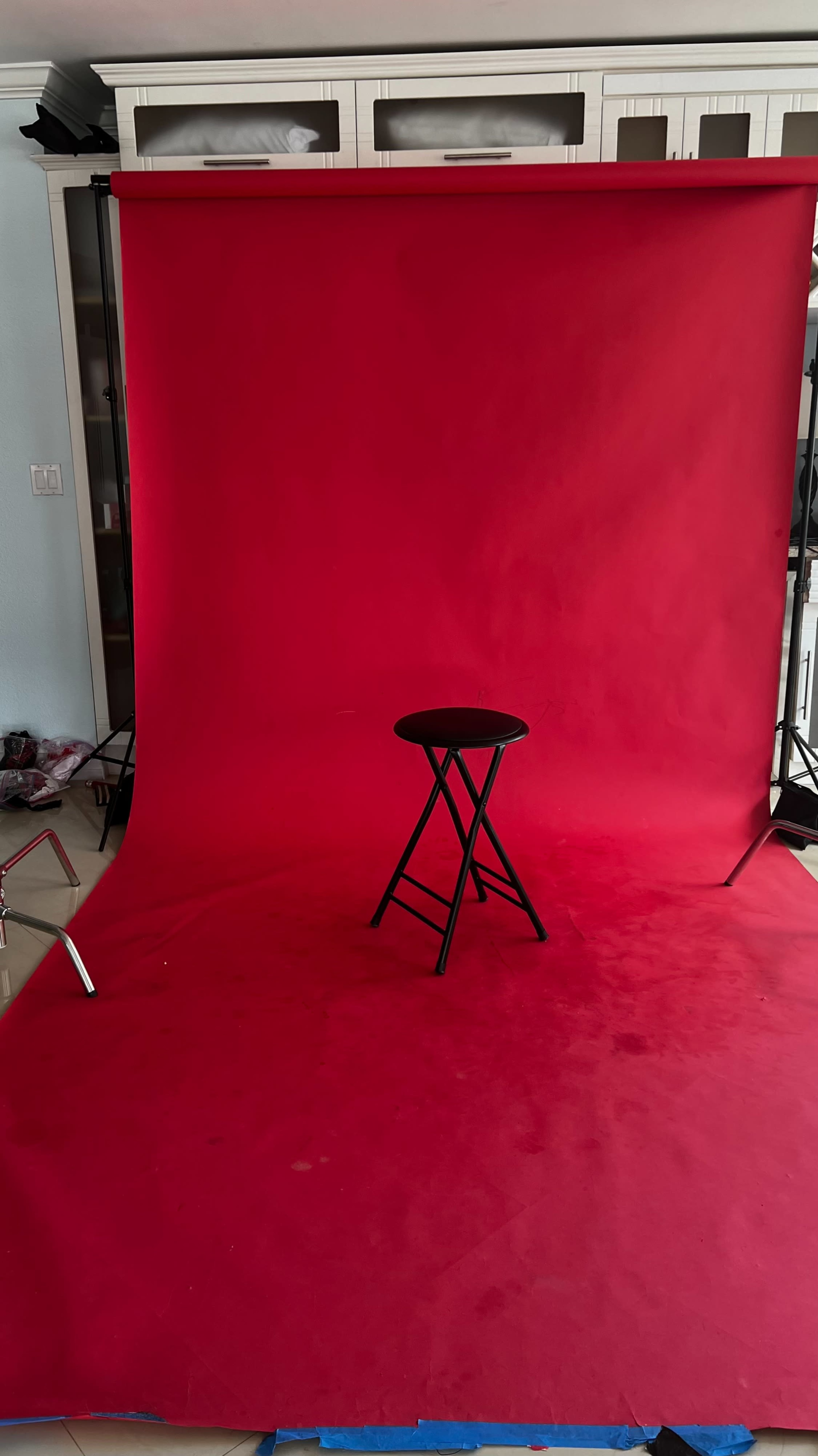 A black stool is placed in front of a red backdrop in a room with visible equipment.