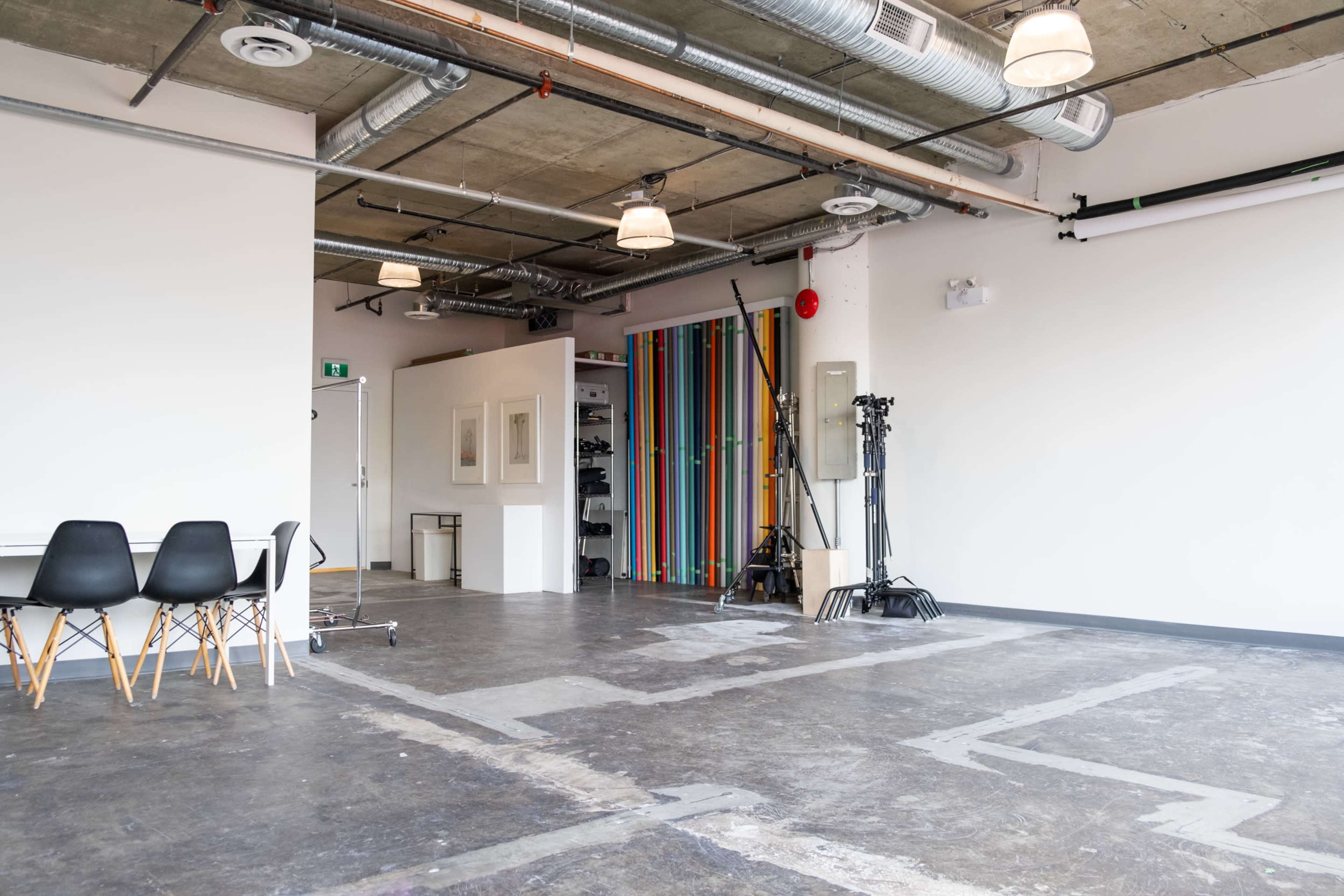An industrial-style studio space with concrete floors, exposed ductwork, and colorful vertical stripes on a partition.