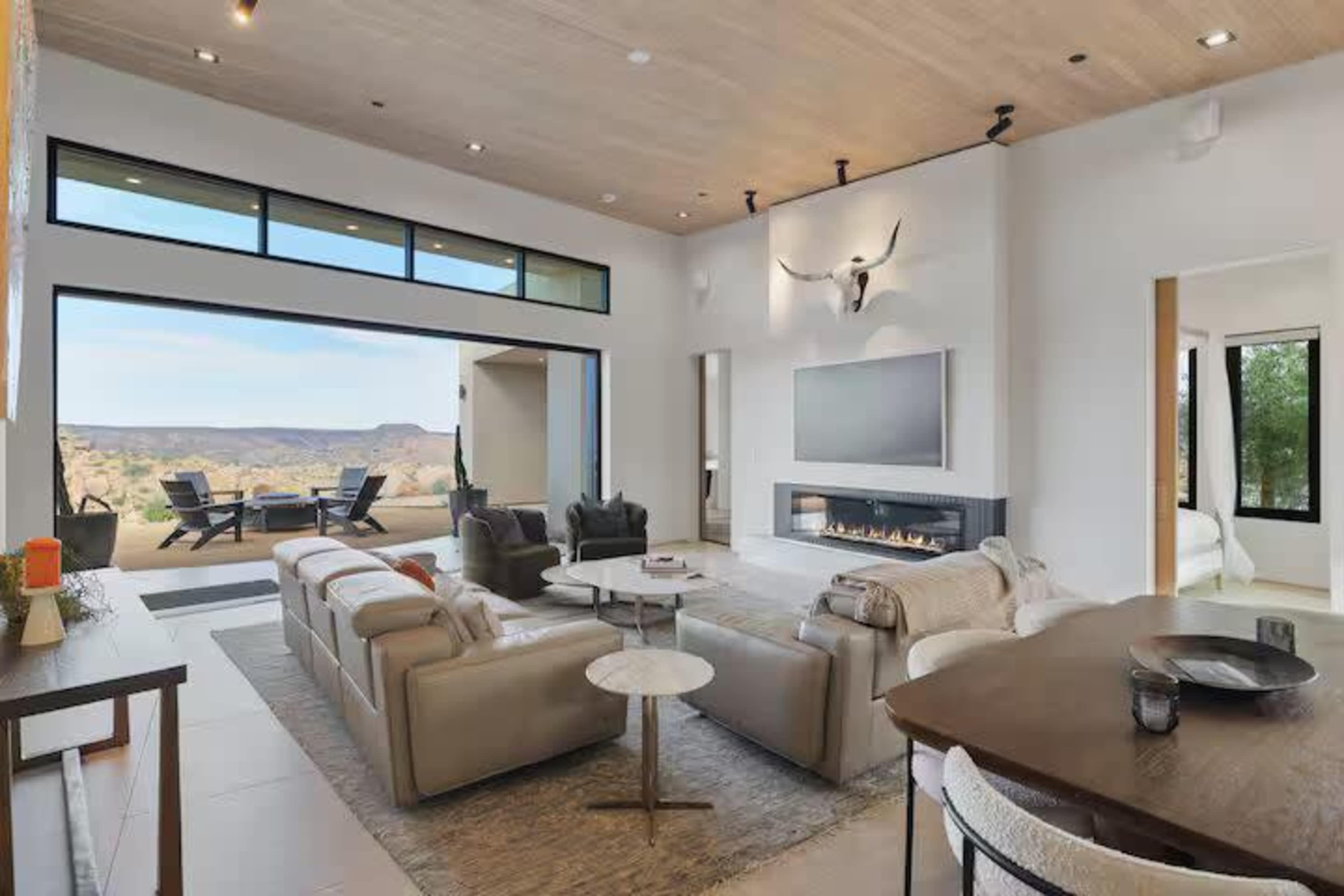 The image shows a modern living room with large windows, a fireplace, and an open view of a desert landscape.