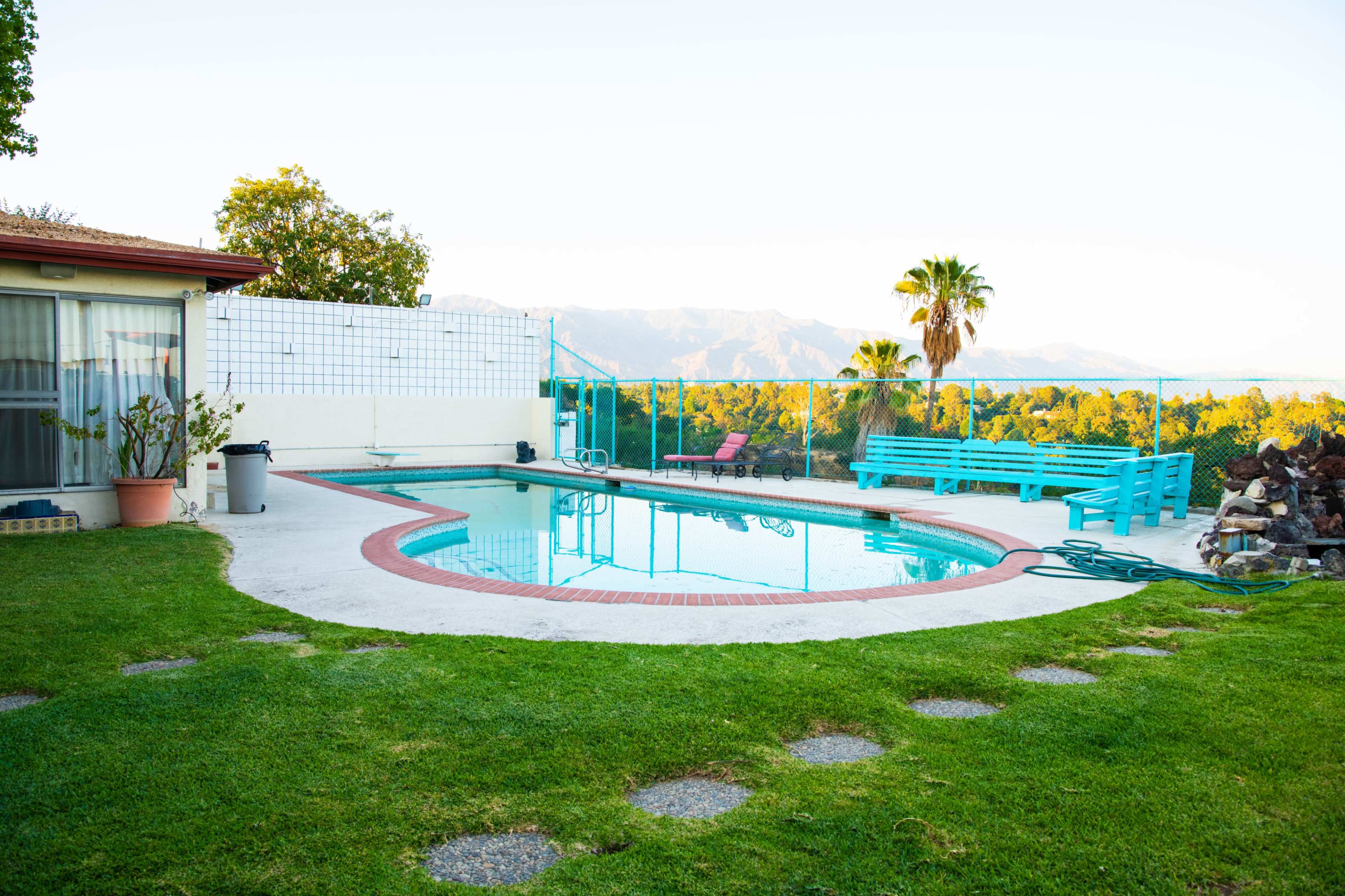 A rectangular swimming pool is surrounded by grass and a patio area, with a fire pit and a view of mountains in the distance.
