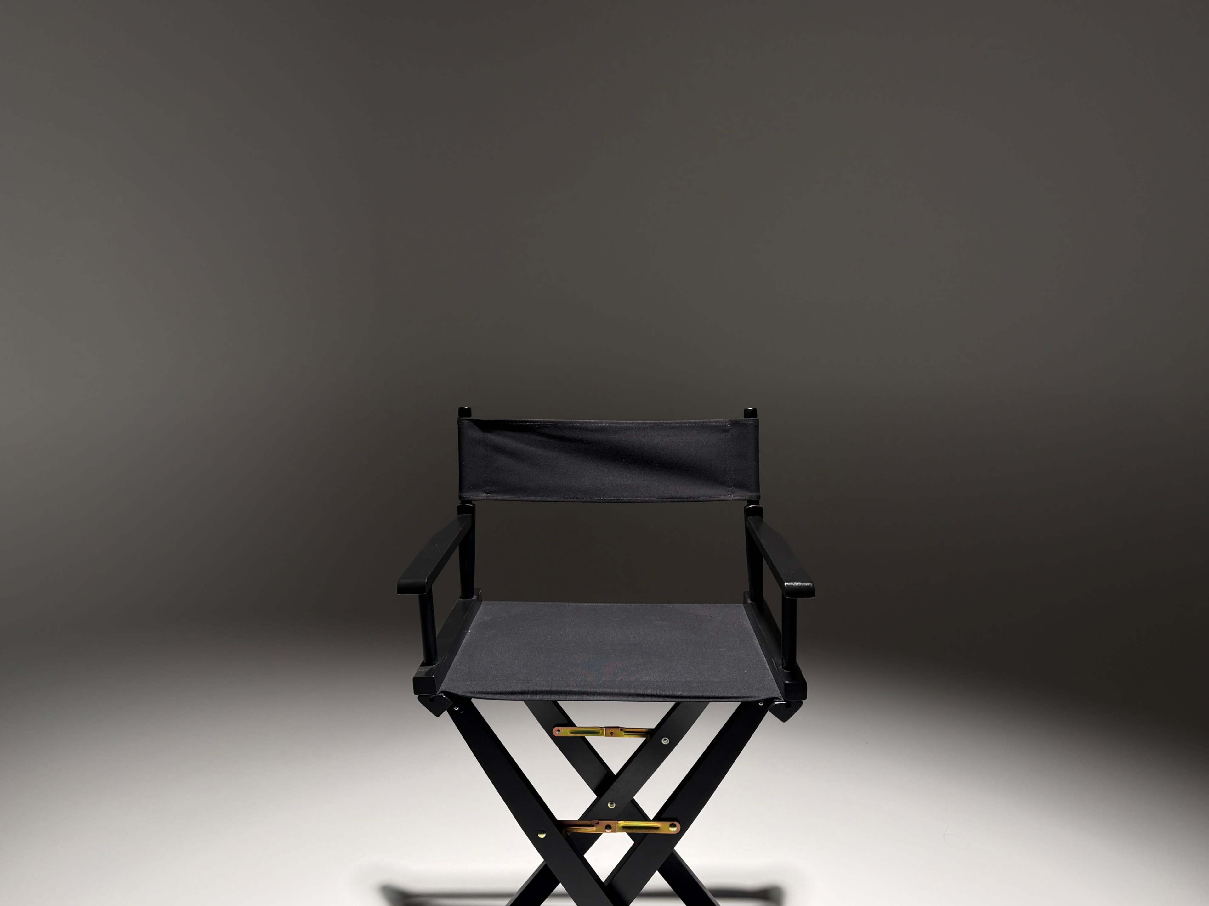 A black director's chair is centered in a dimly lit space with a grey background.