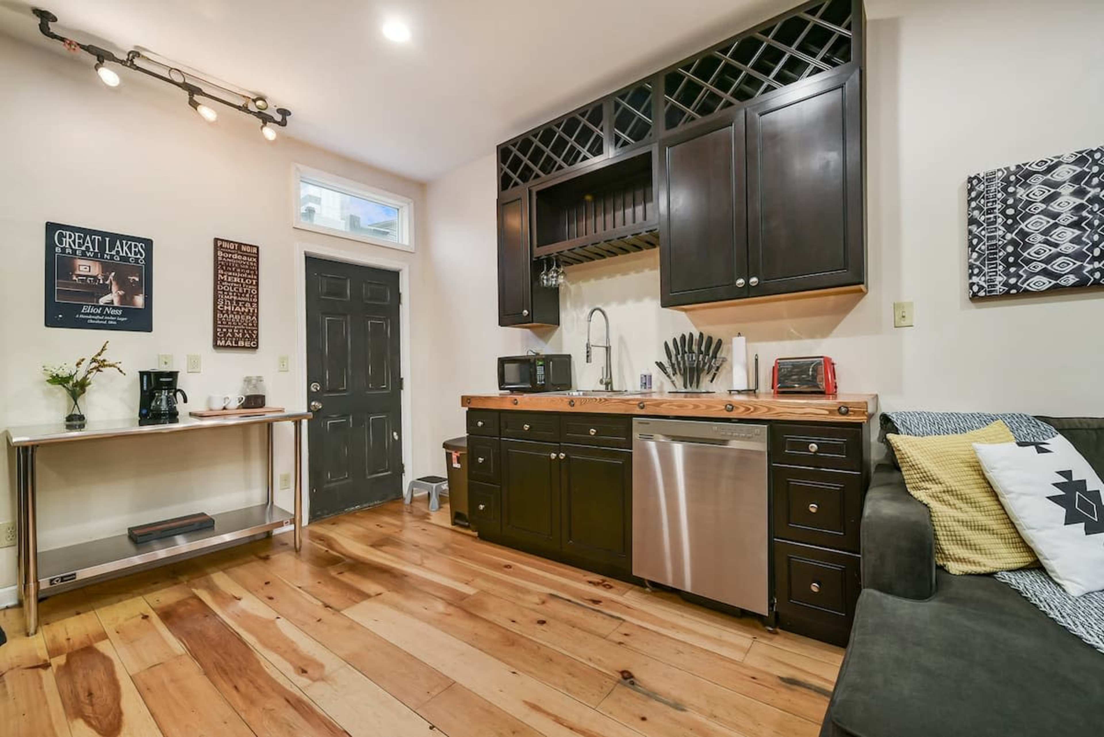 A cozy kitchenette with dark cabinets, a stainless steel sink, and wooden countertops, adjacent to a living area with light wooden flooring.