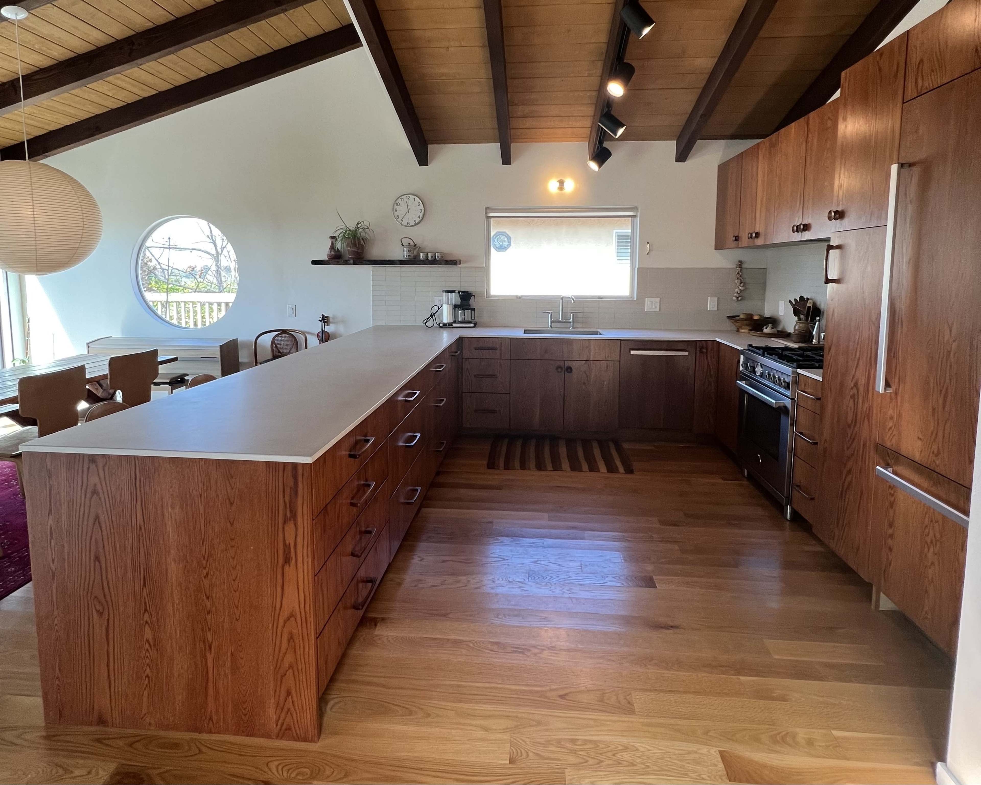 The kitchen features wooden cabinets, a large island with a countertop, and a round window, creating an open and modern space.