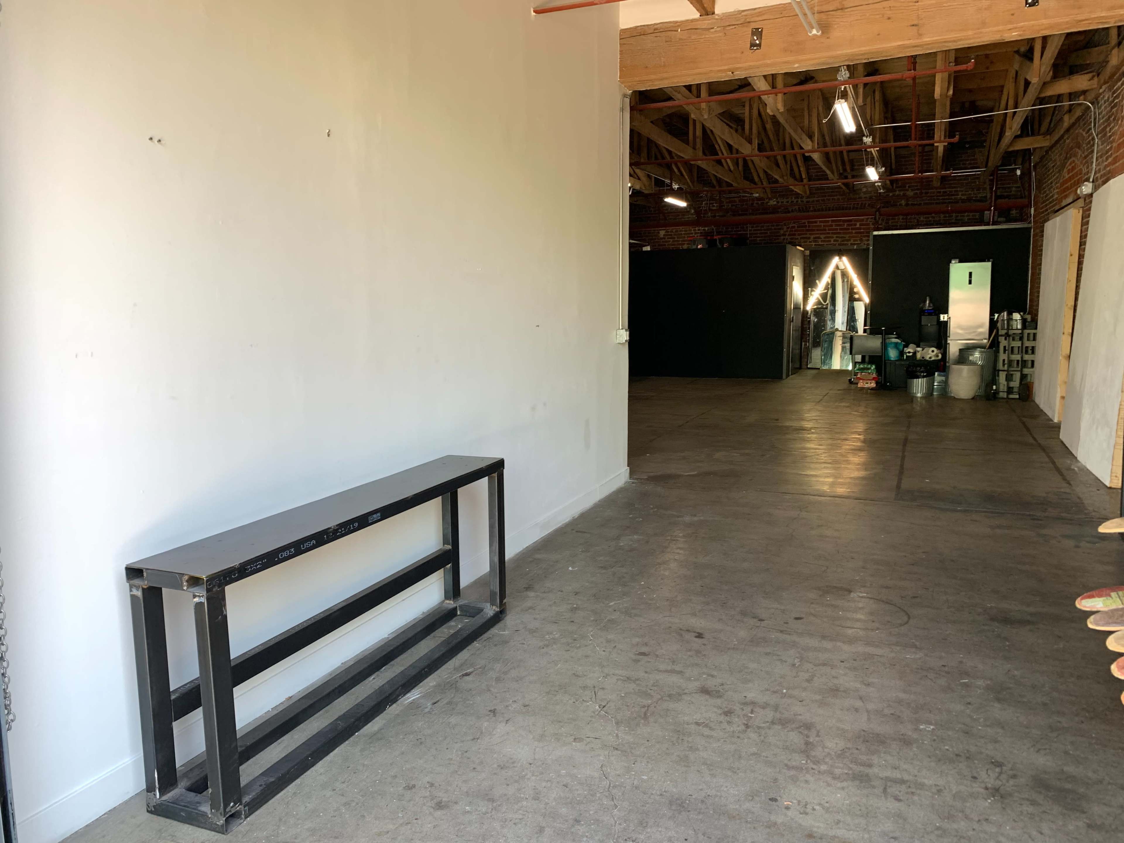 A spacious, empty room with a metal table against a white wall and a dark area visible in the background.