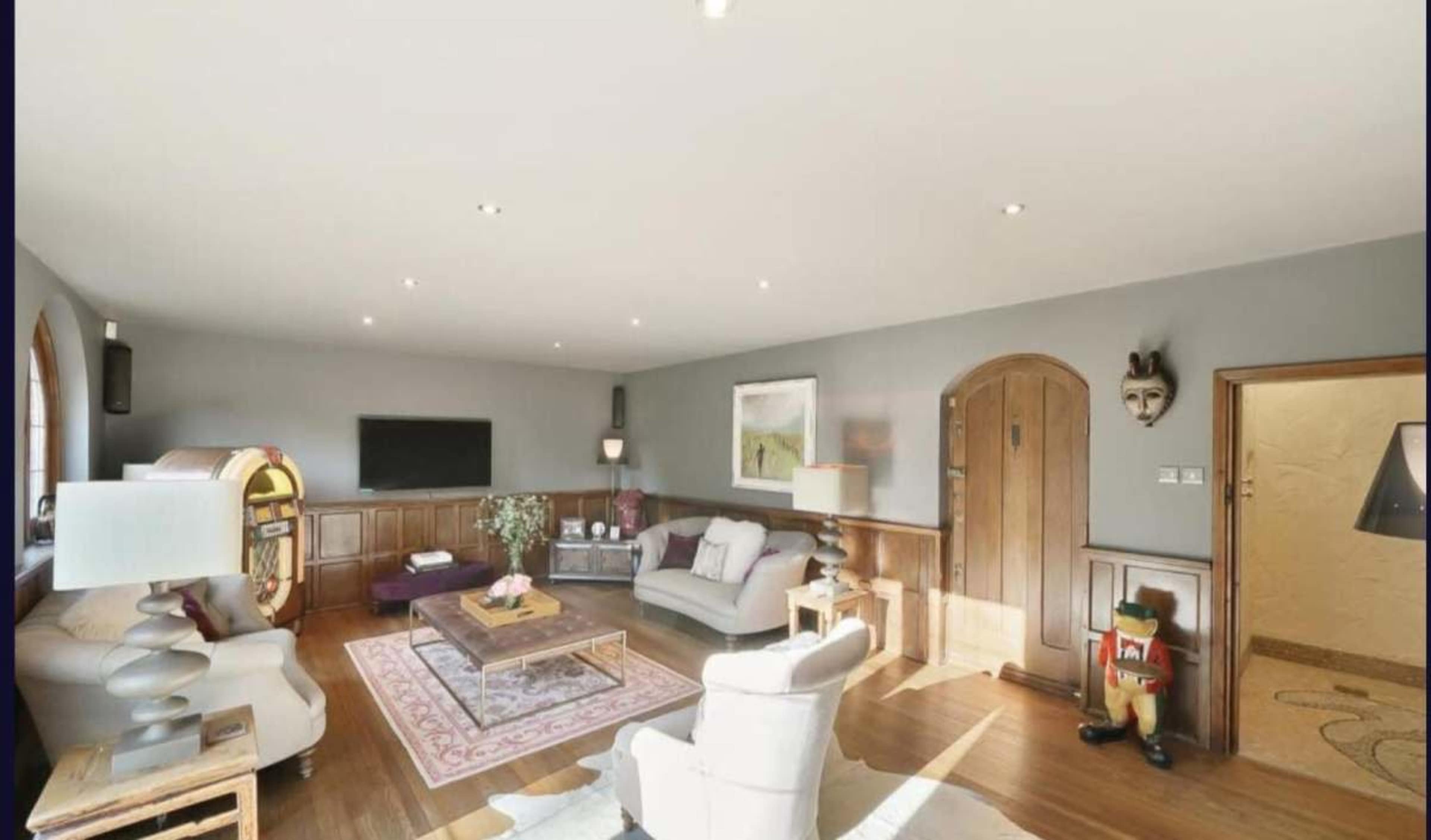 The image shows a modern living room with a light color scheme, wooden accents, and a mix of furniture including sofas, a coffee table, and decorative items.