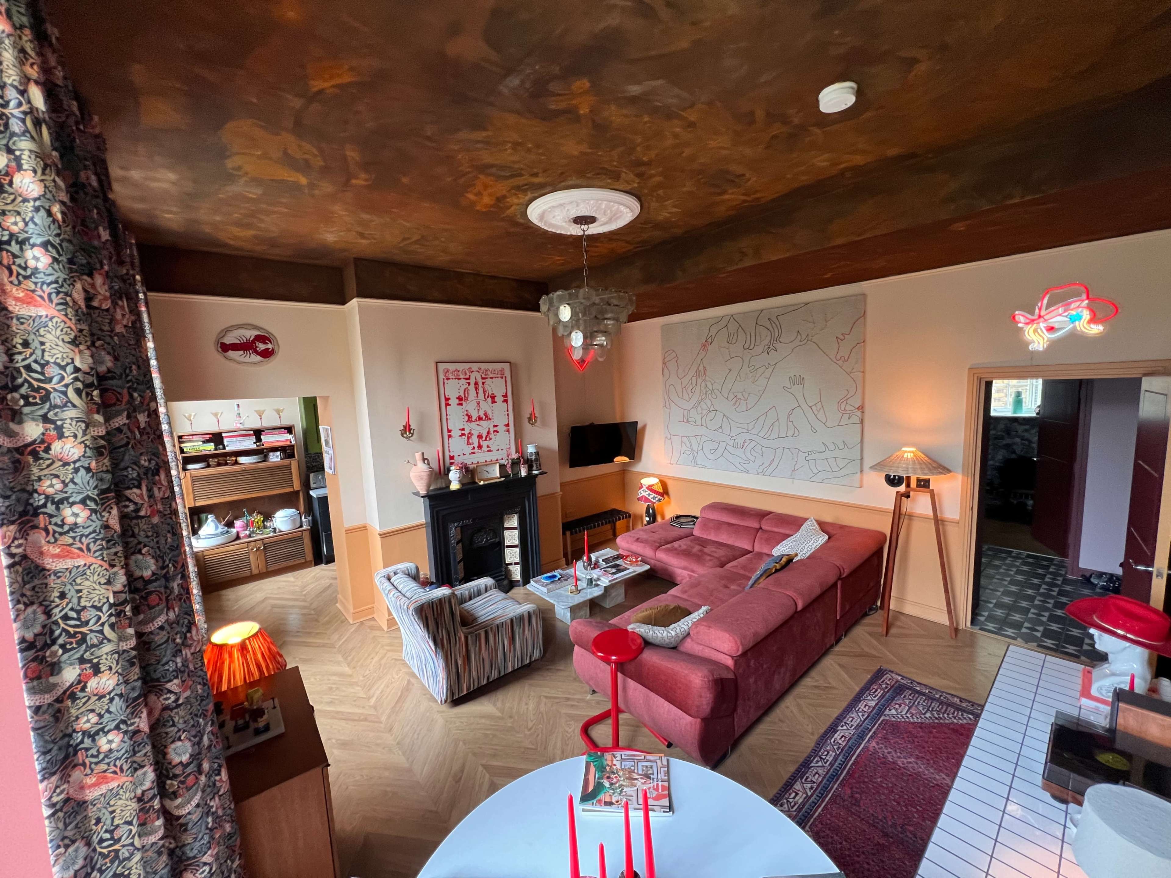 A cozy living room featuring a pink sofa, a large wall art piece, a television on a mantle, and various decorative elements.