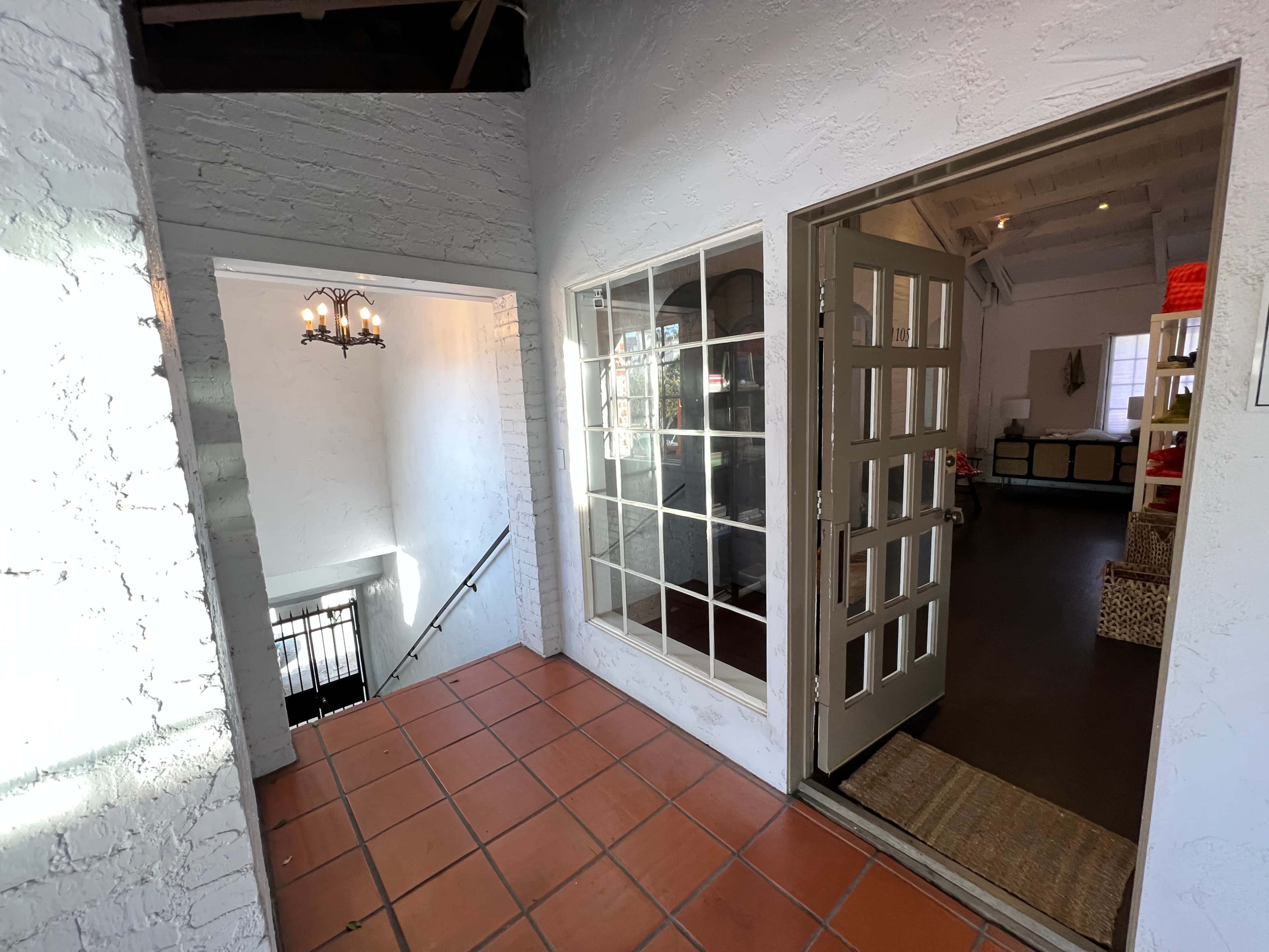 The image shows a hallway with a doorway leading to a room and a staircase descending to another level, featuring tiled flooring and white walls.