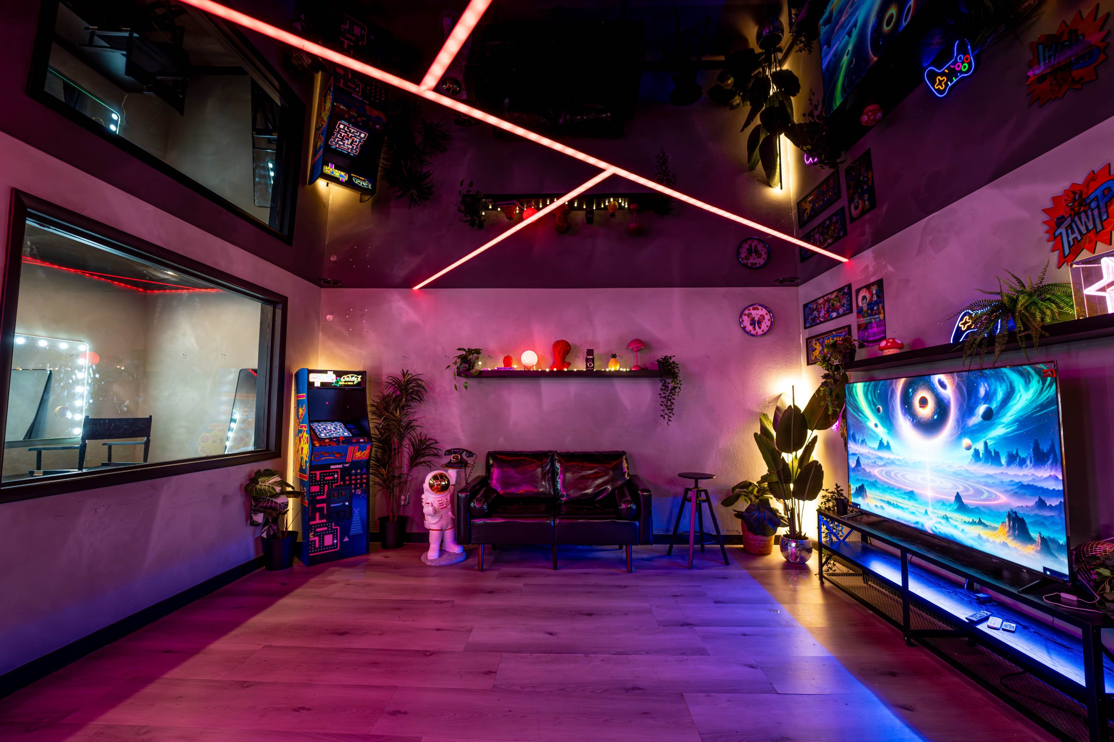 The image depicts a modern gaming room featuring a sleek couch, a large TV displaying vibrant graphics, neon lighting, and various gaming-related decor on the walls.