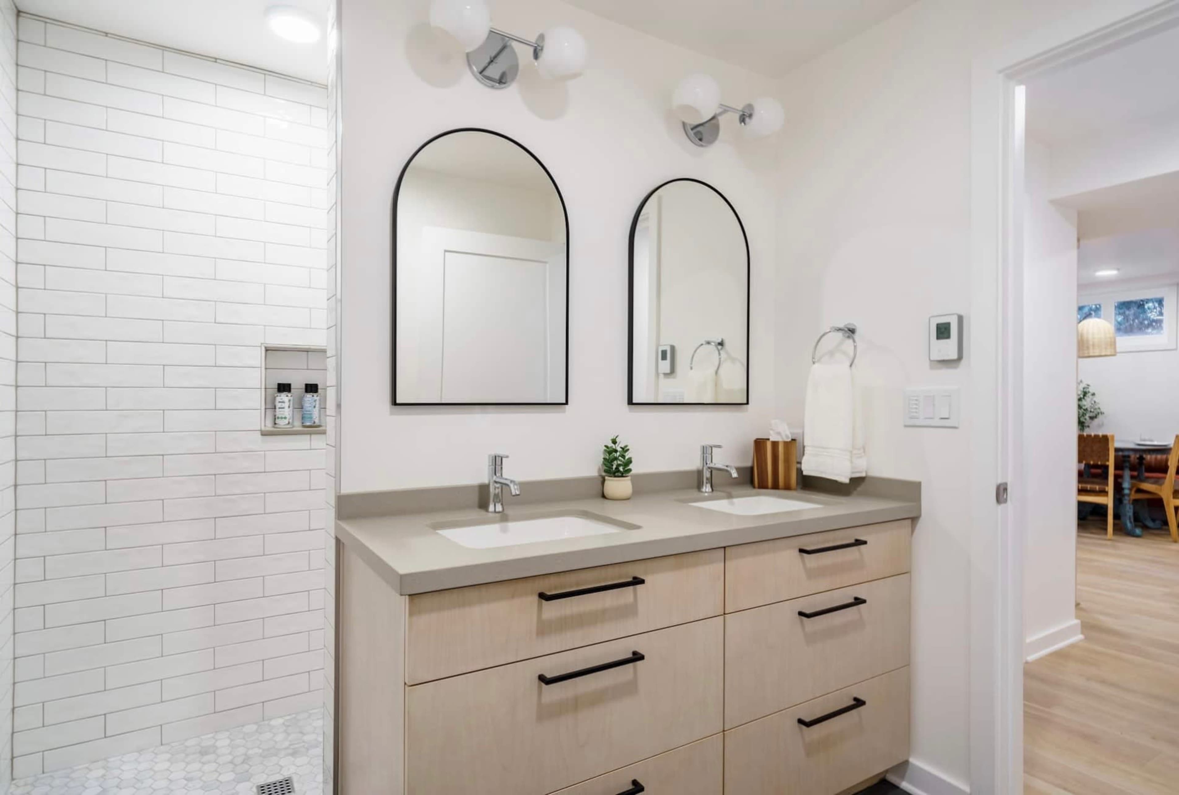 A modern bathroom featuring a double vanity with two sinks, large mirrors, and a walk-in shower with tiled walls.