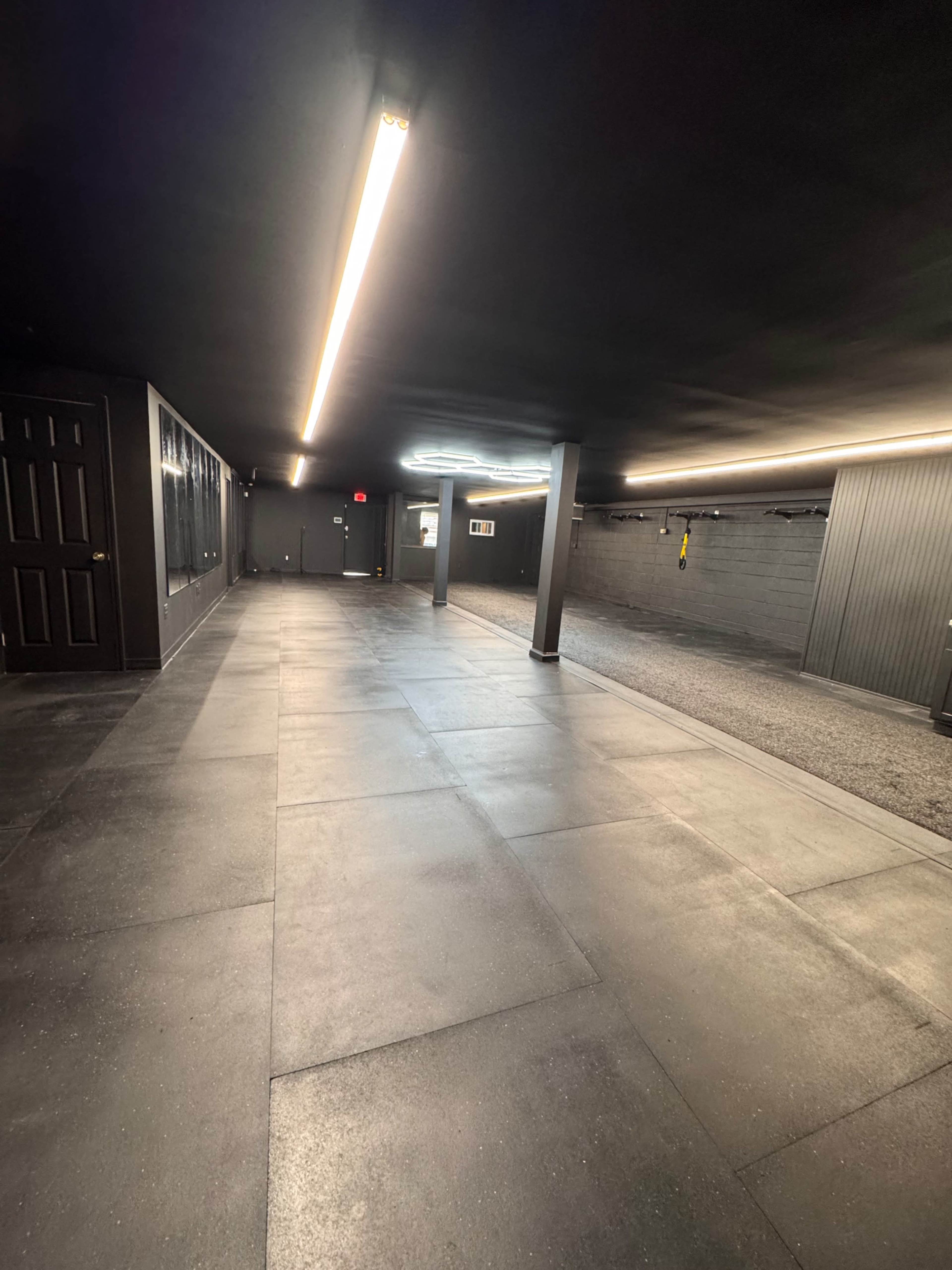 The image shows a long, narrow room with a dark ceiling and walls, illuminated by ceiling-mounted fluorescent lights.