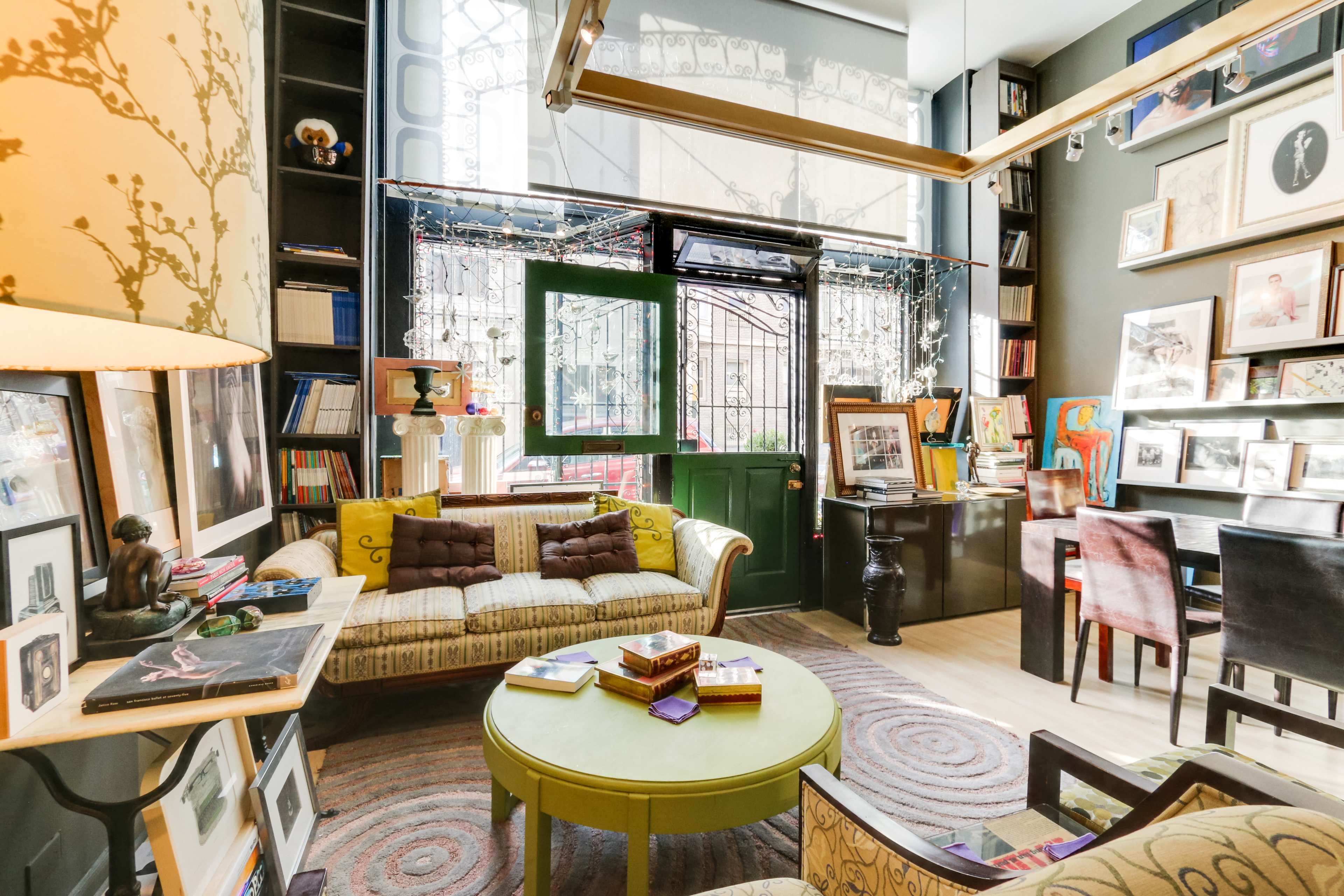 A cozy room with a green door, a patterned sofa, a round coffee table, and walls decorated with framed pictures and bookshelves.