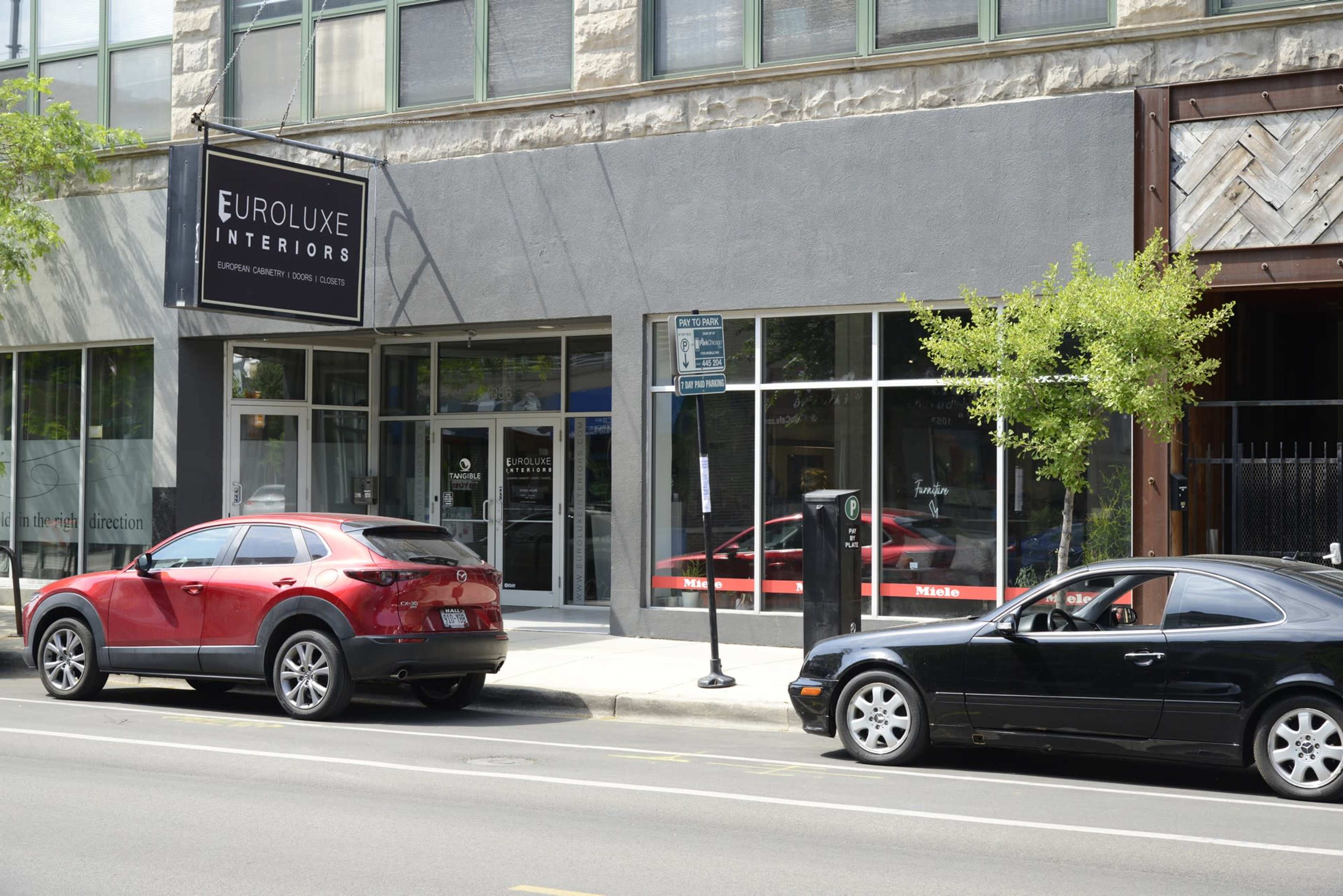 The image shows a modern building facade featuring a sign for "Euroluxe Interiors," with two cars parked on the street in front.