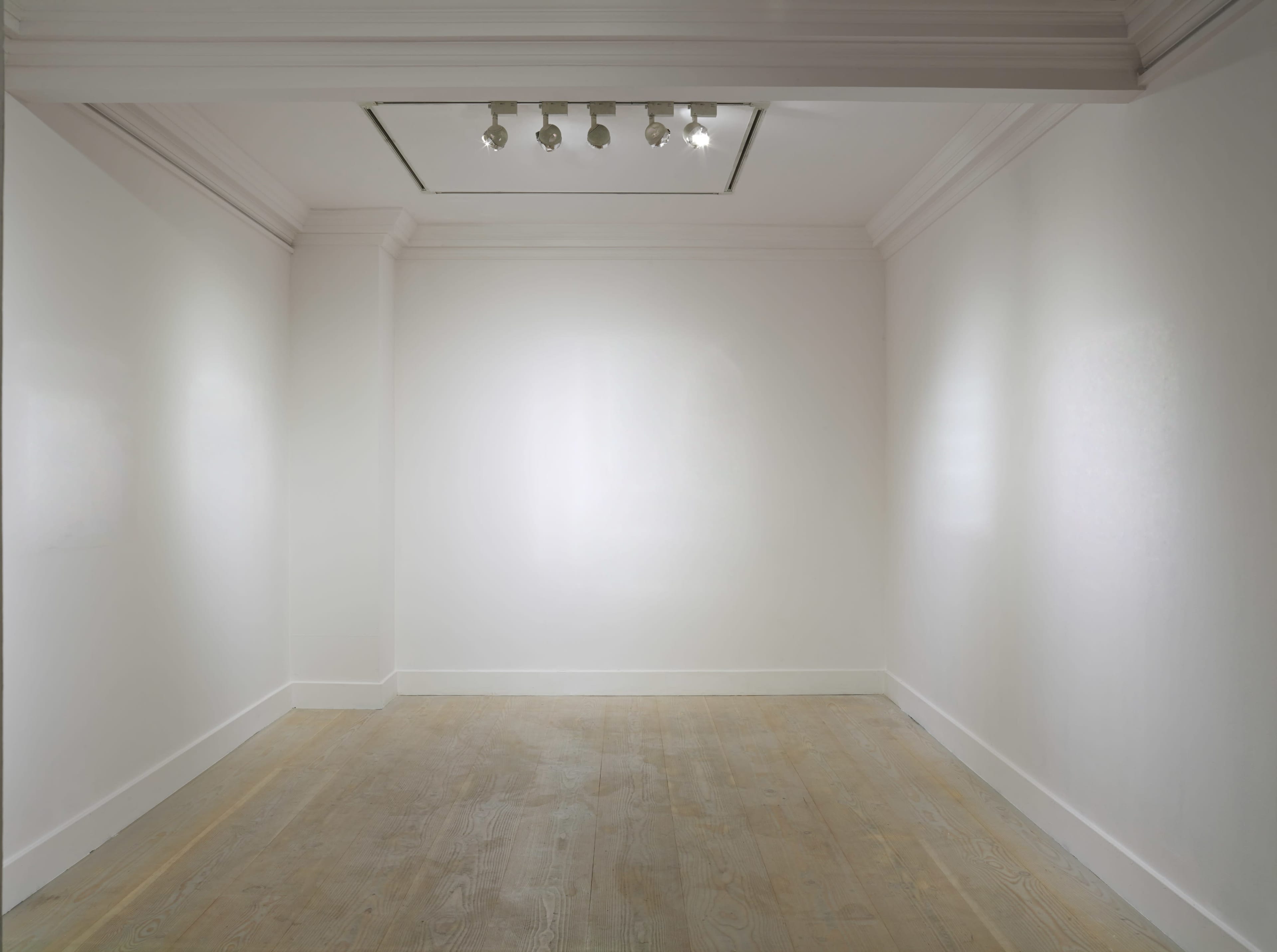 An empty, well-lit gallery space with white walls and a wooden floor.