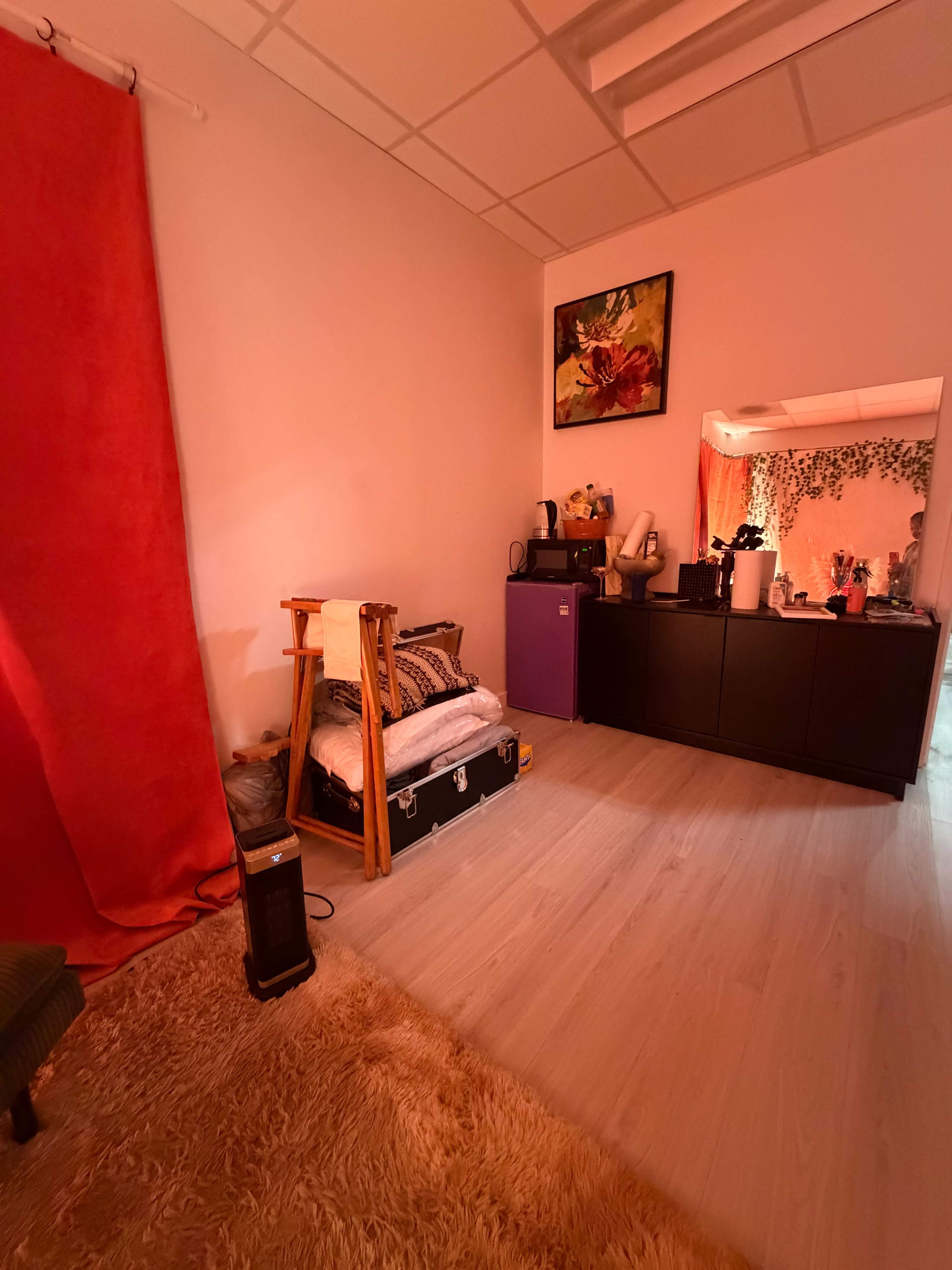 The image shows a small room with a red curtain, a bed on a wooden frame, a dresser against the wall, and various decorative items.