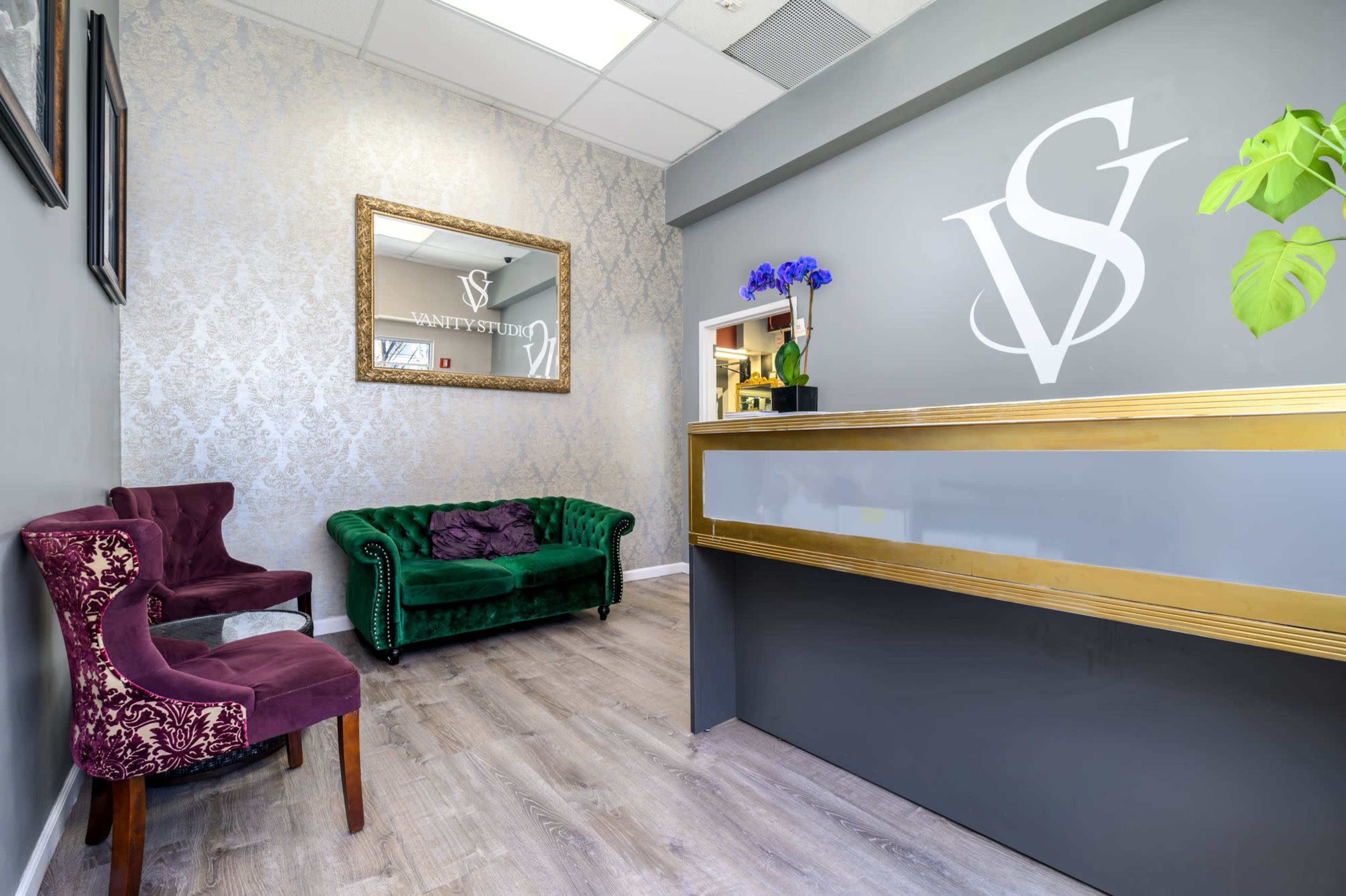 A modern reception area with a green velvet couch, two chairs, and a front desk featuring a large mirror and decorative elements.