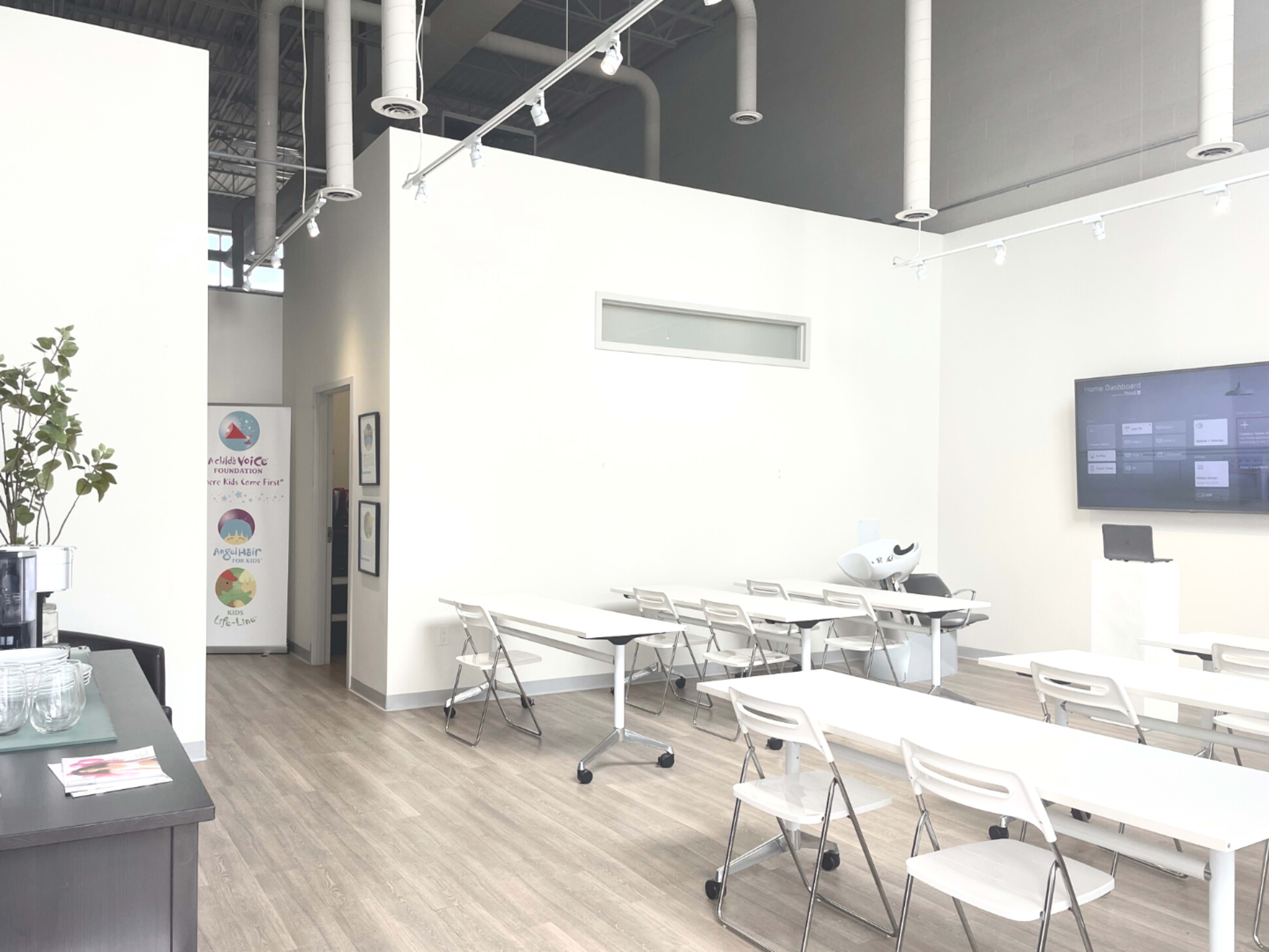 A modern, spacious office environment with white walls, a few tables and chairs, and a digital screen on one wall.