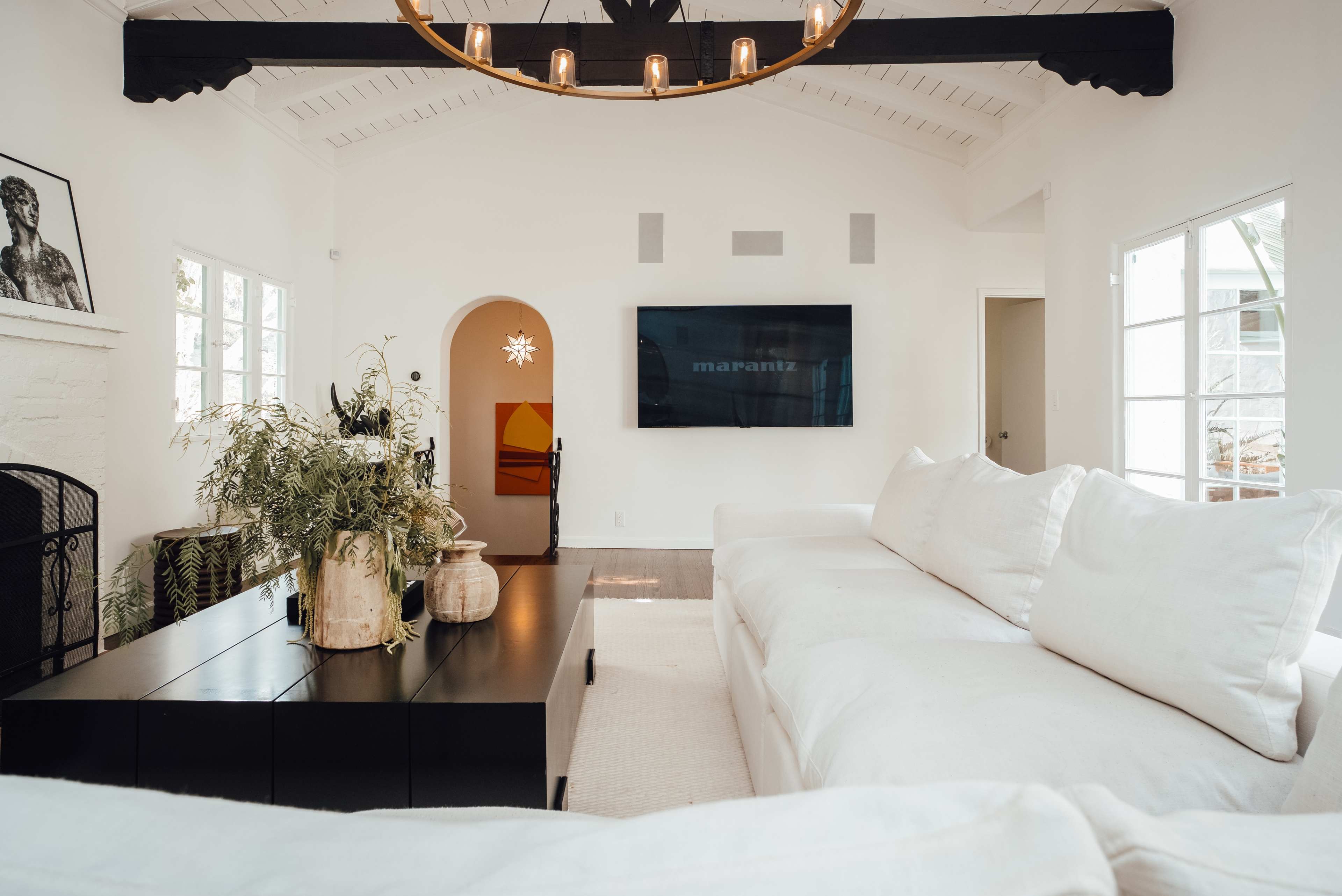 A bright, minimalist living room features a large white sectional sofa, a black media unit, and a mounted television on a white wall.