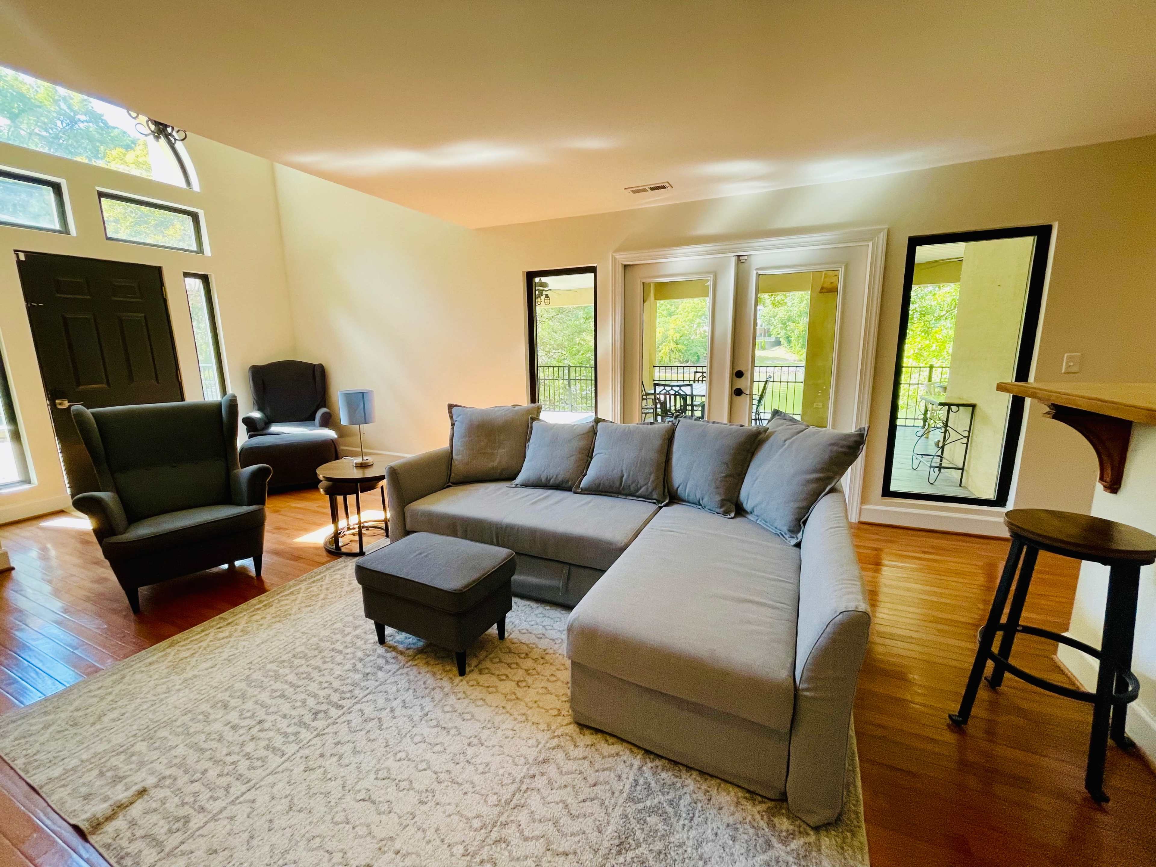 The room features a sectional sofa, a coffee table, and a couple of chairs with large windows that provide views of the outdoors.
