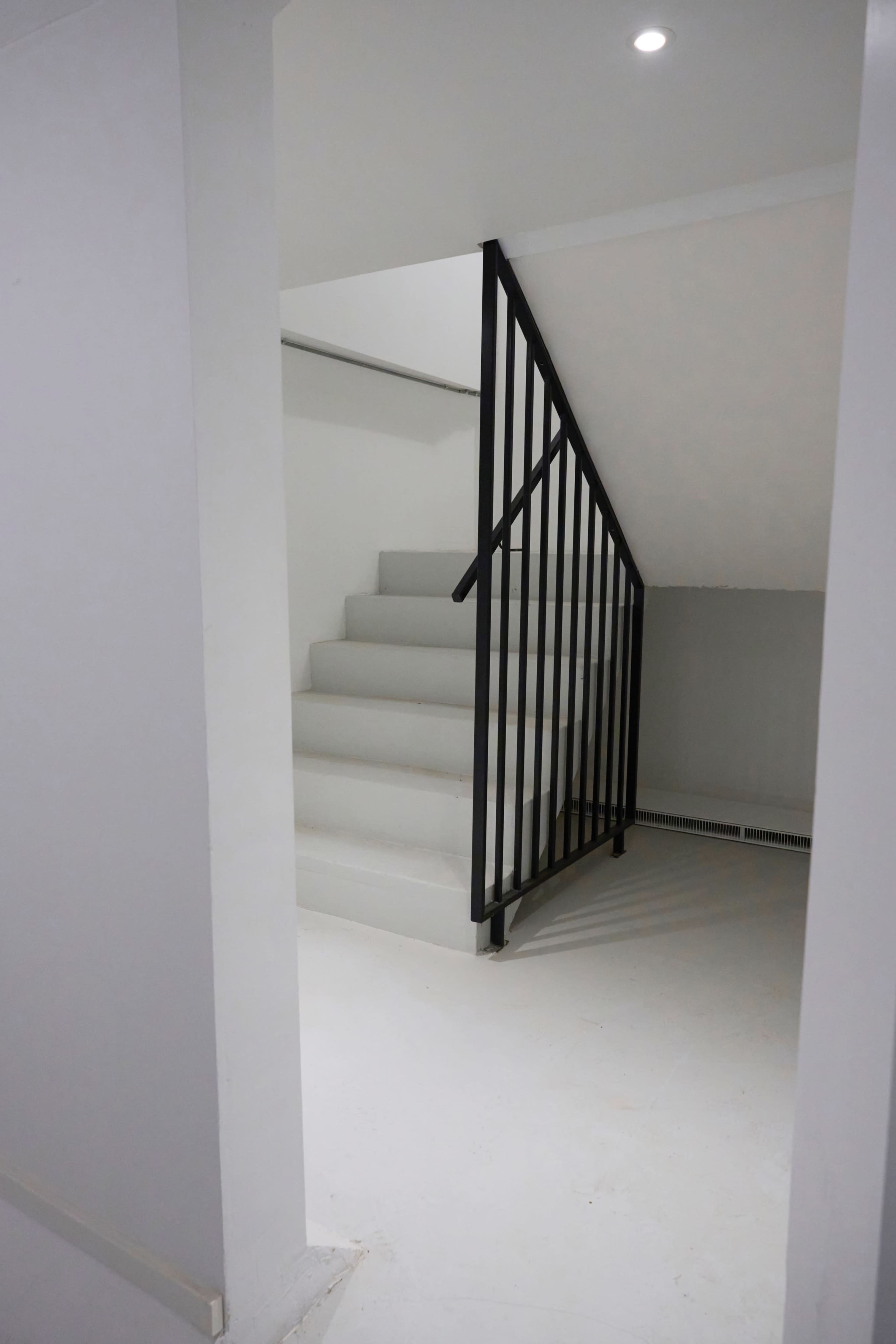 A staircase leading to an upper level, enclosed by a black metal railing, in a minimalist interior hallway.