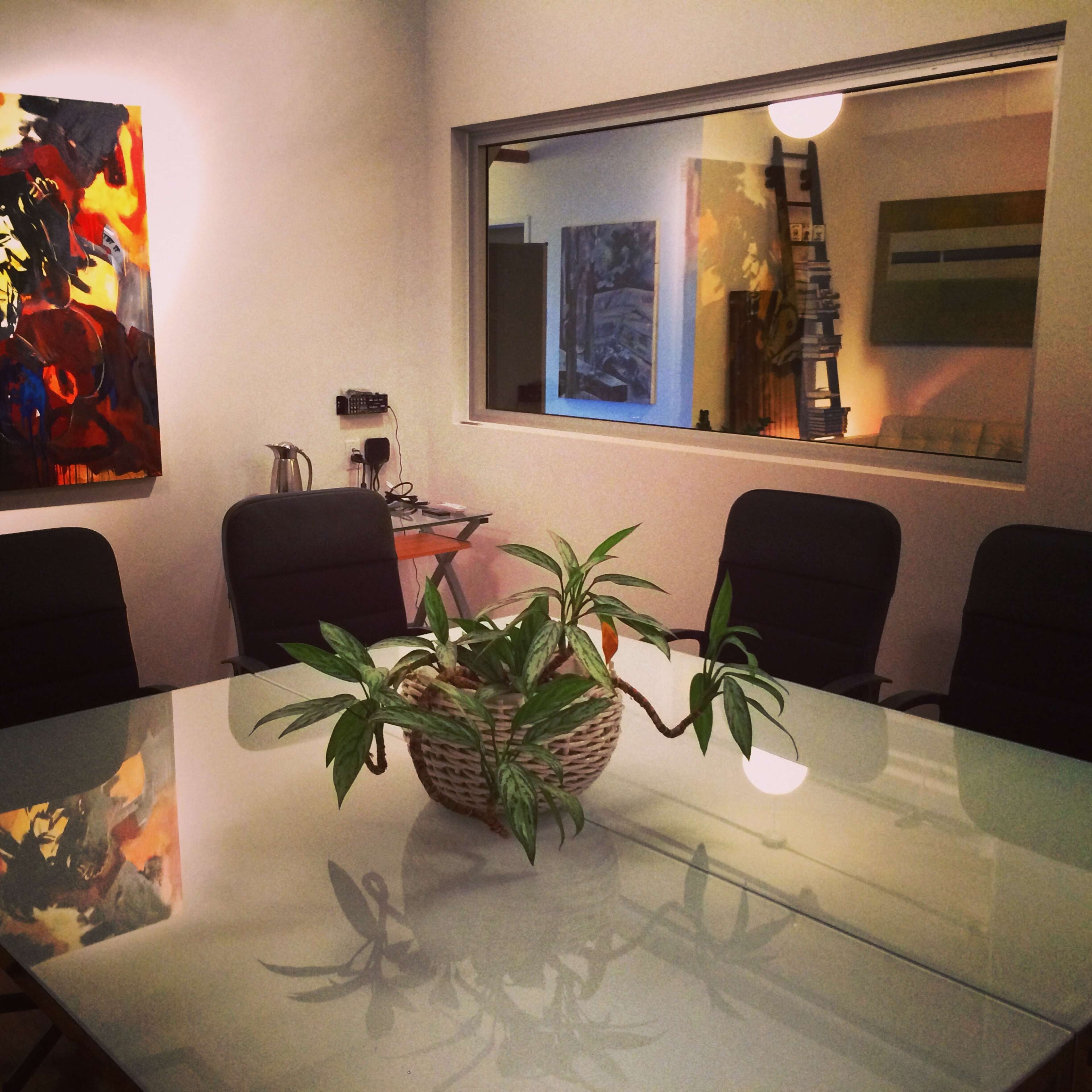 A glass conference table is surrounded by black chairs in a room with colorful artwork on the walls.