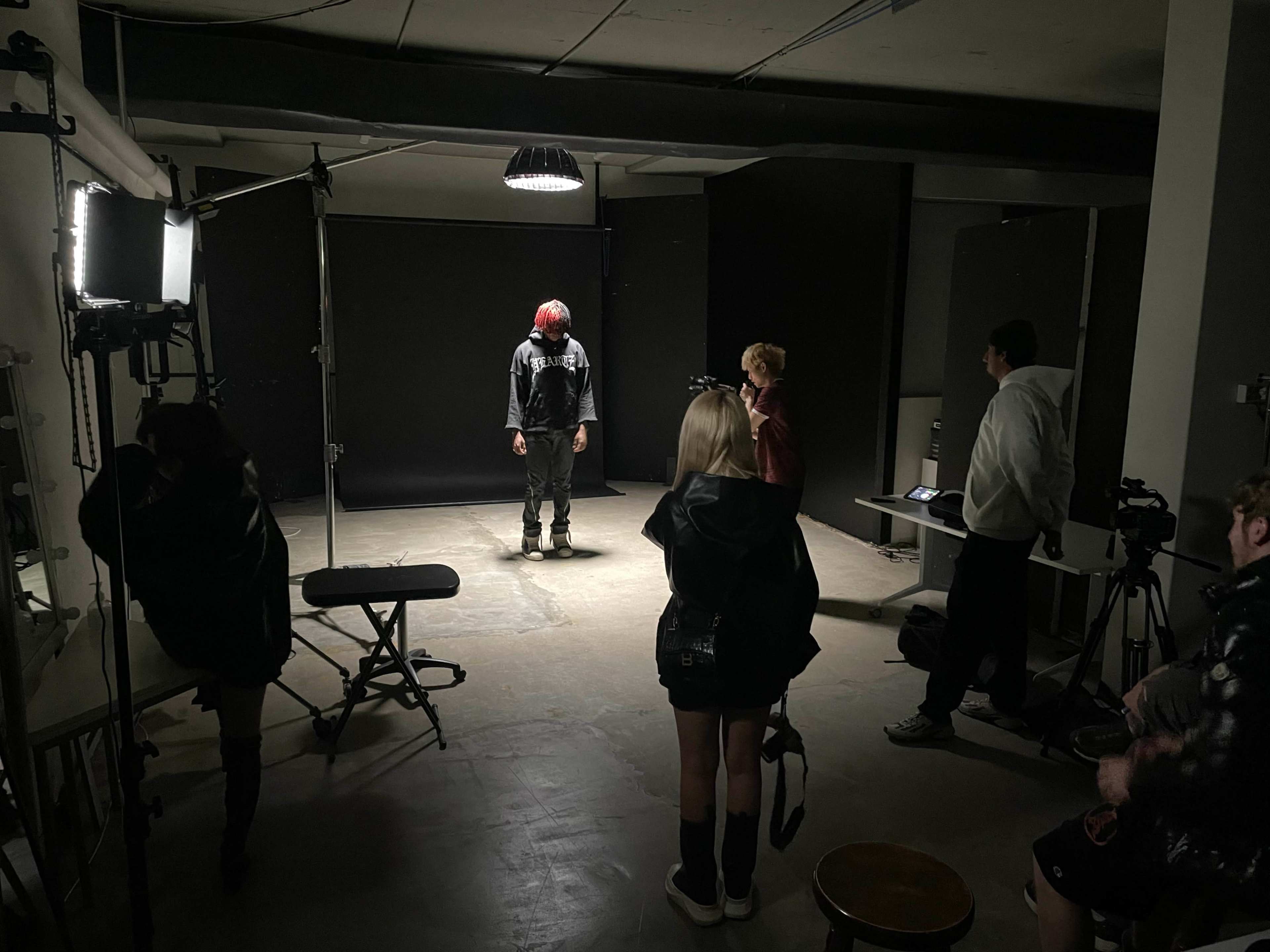 A group of individuals observes a person standing under a spotlight in a photography studio.