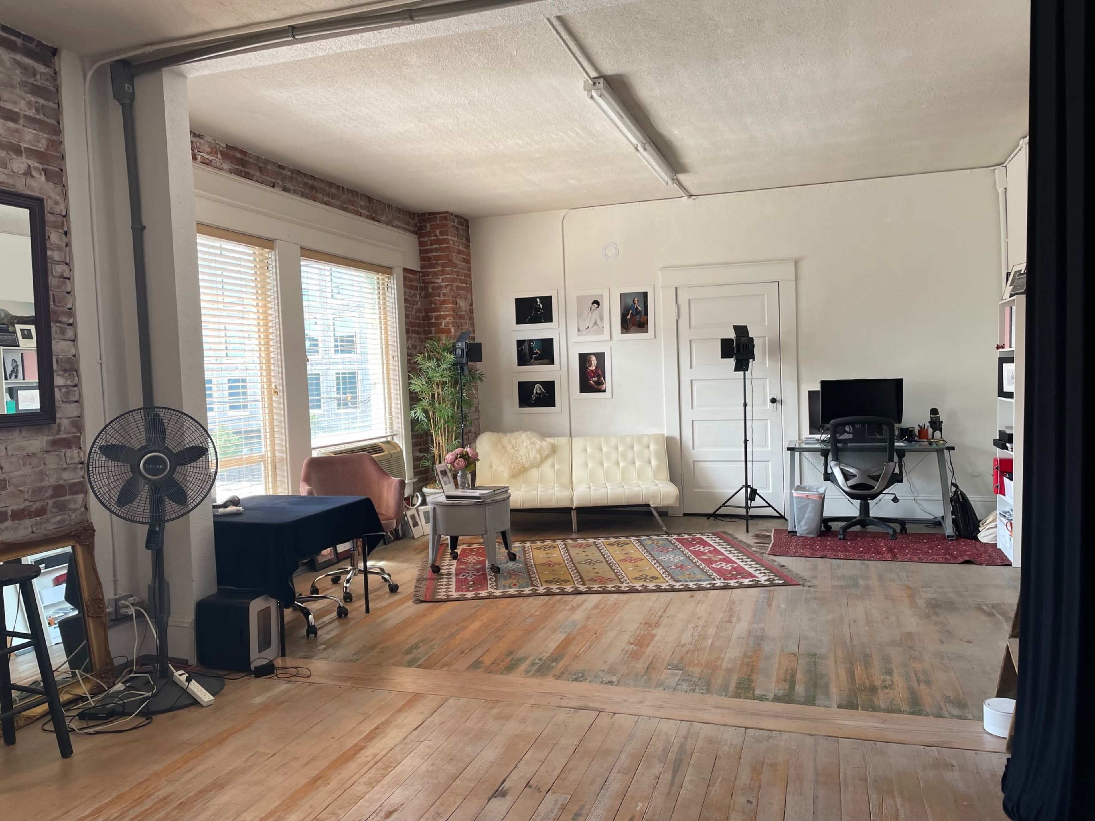 A spacious room with exposed brick walls, a white couch, a desk, a computer setup, and decorative photos on the walls.