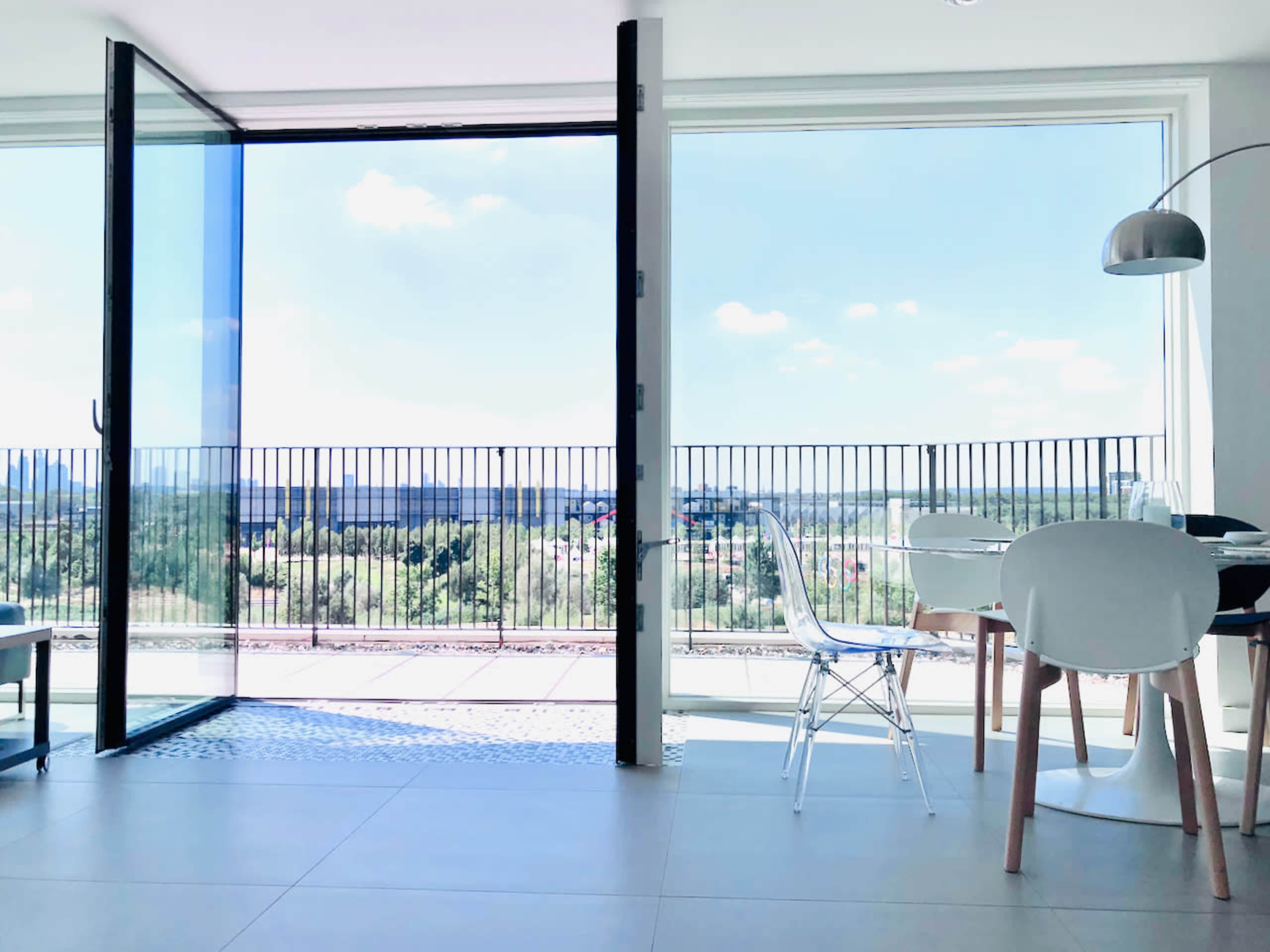 A modern dining area features a large glass door opening to a balcony with a view of the landscape beyond.
