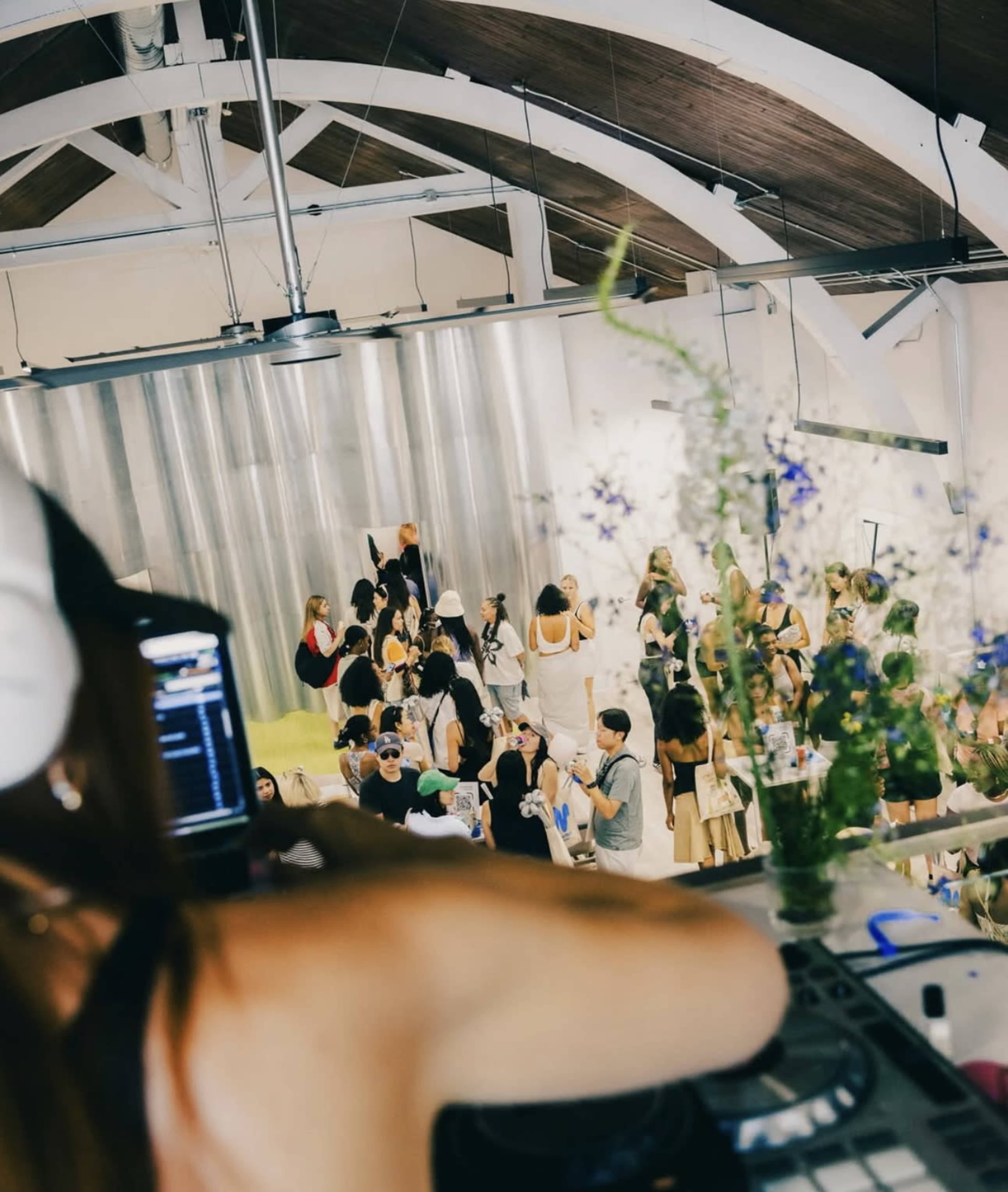 A DJ plays music at a lively event while guests socialize and dance in a spacious venue.