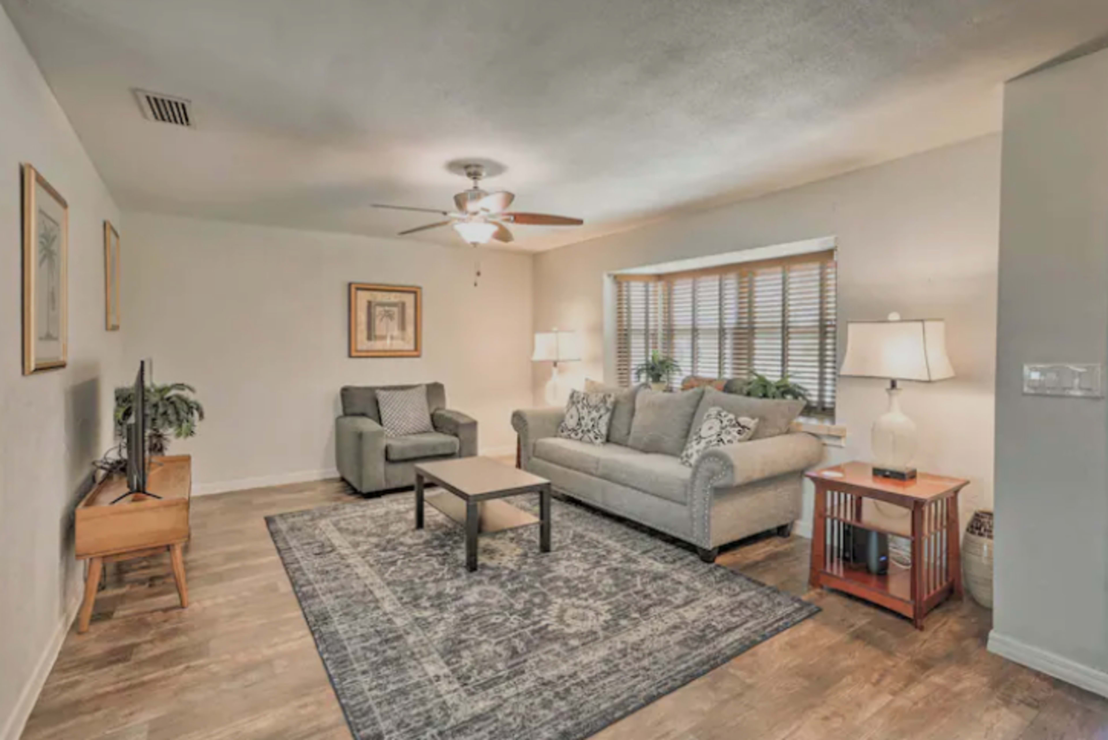 The living room features a sofa, a chair, a coffee table, and a television, with wooden flooring and light-colored walls.