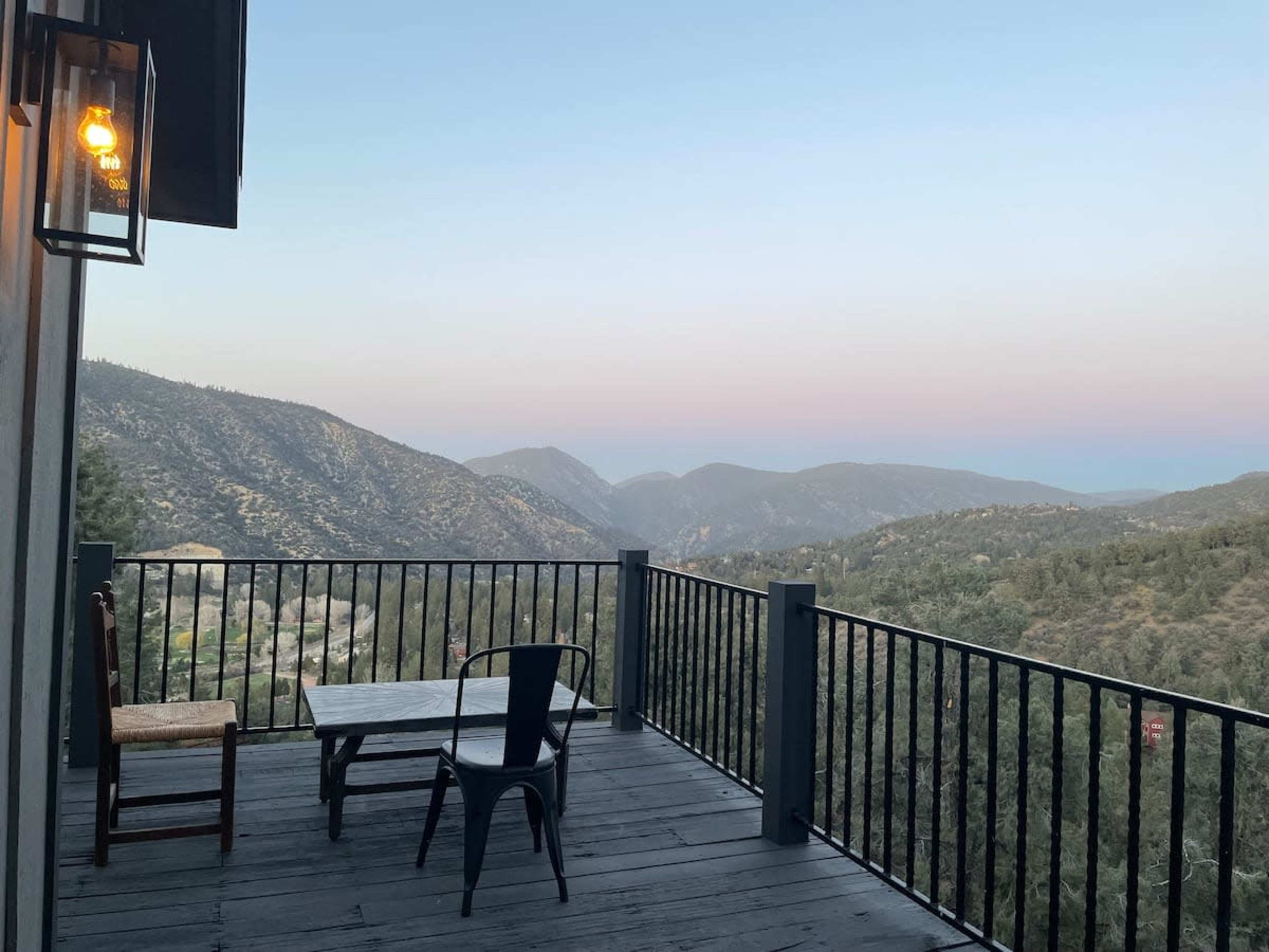A wooden deck overlooking mountains during twilight, featuring a table and two chairs.